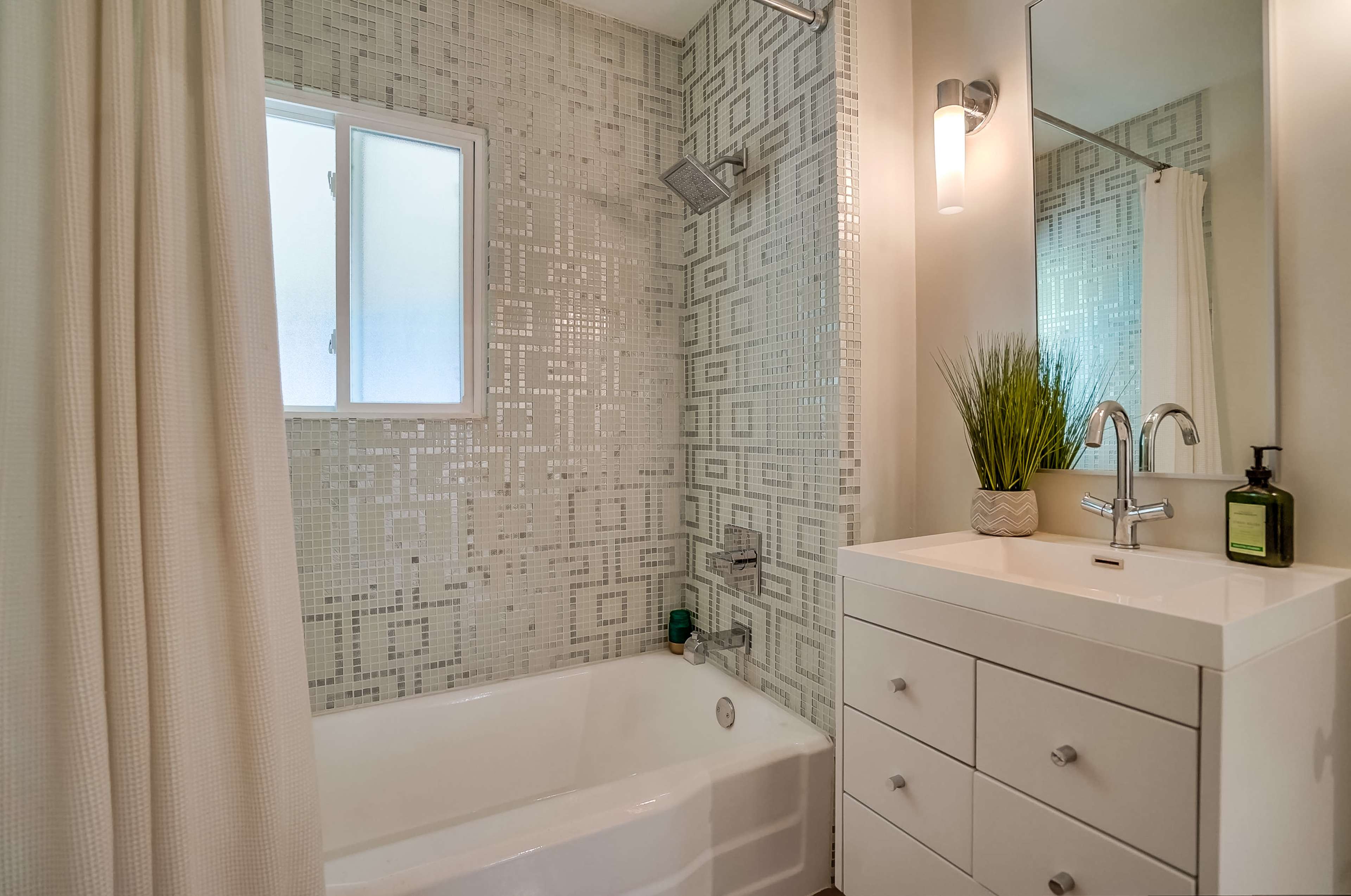 The bathroom features a tub with a tiled backsplash, a wall-mounted shower, and a sink with a modern, minimalist cabinet.