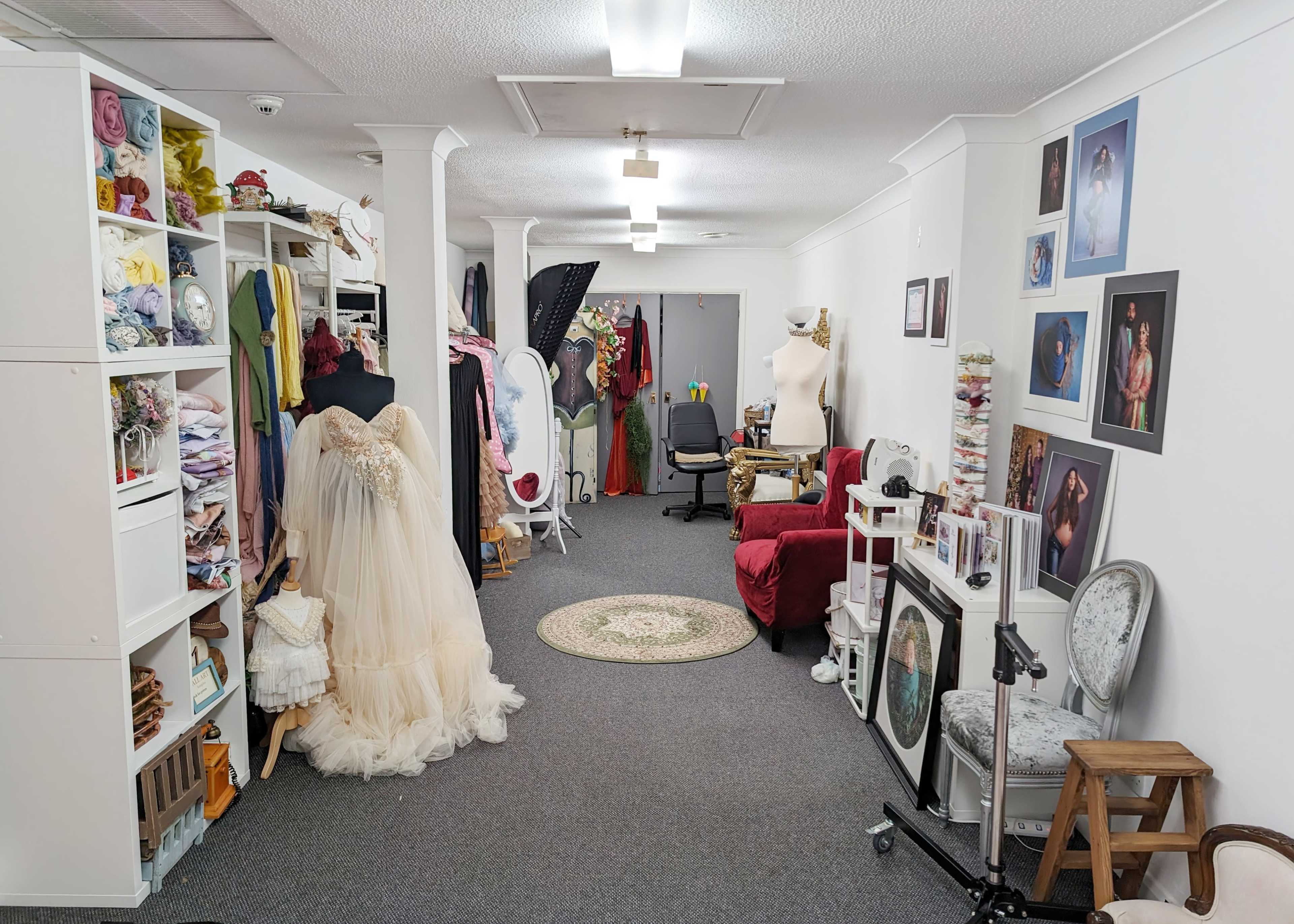 A spacious dressmaking studio featuring a variety of colorful fabrics, a mannequin dressed in a formal gown, and numerous photos and props arranged throughout the room.