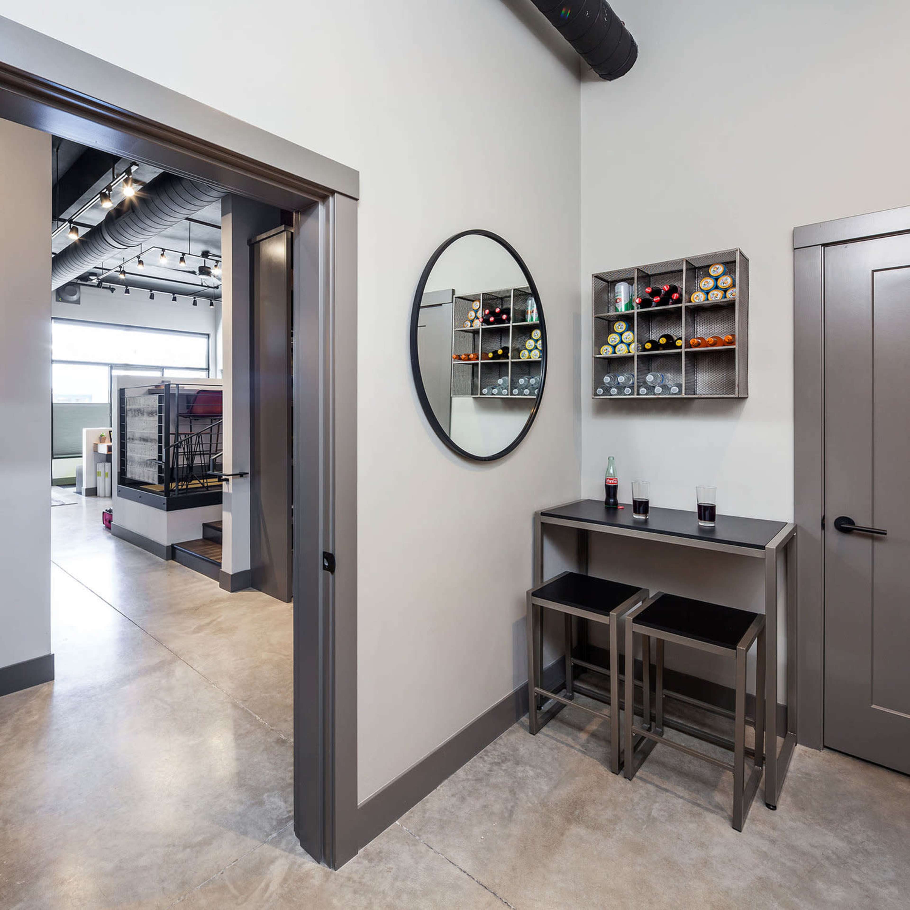 A modern hallway with a round mirror, a wall-mounted wine rack displaying several bottles, and a small table with two stools.