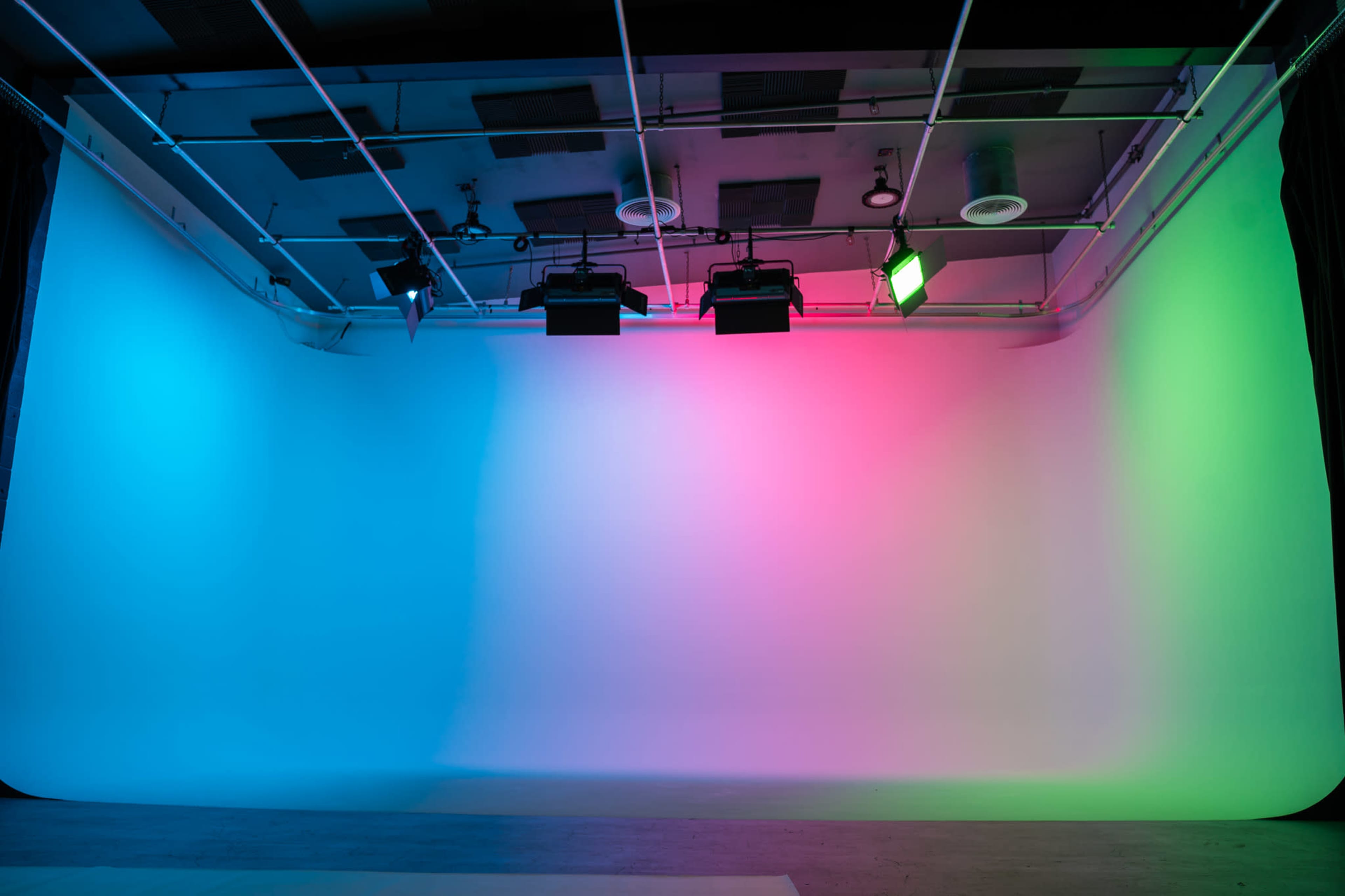 The image shows a studio with a large, gradient backdrop illuminated by colorful lighting from overhead spots.