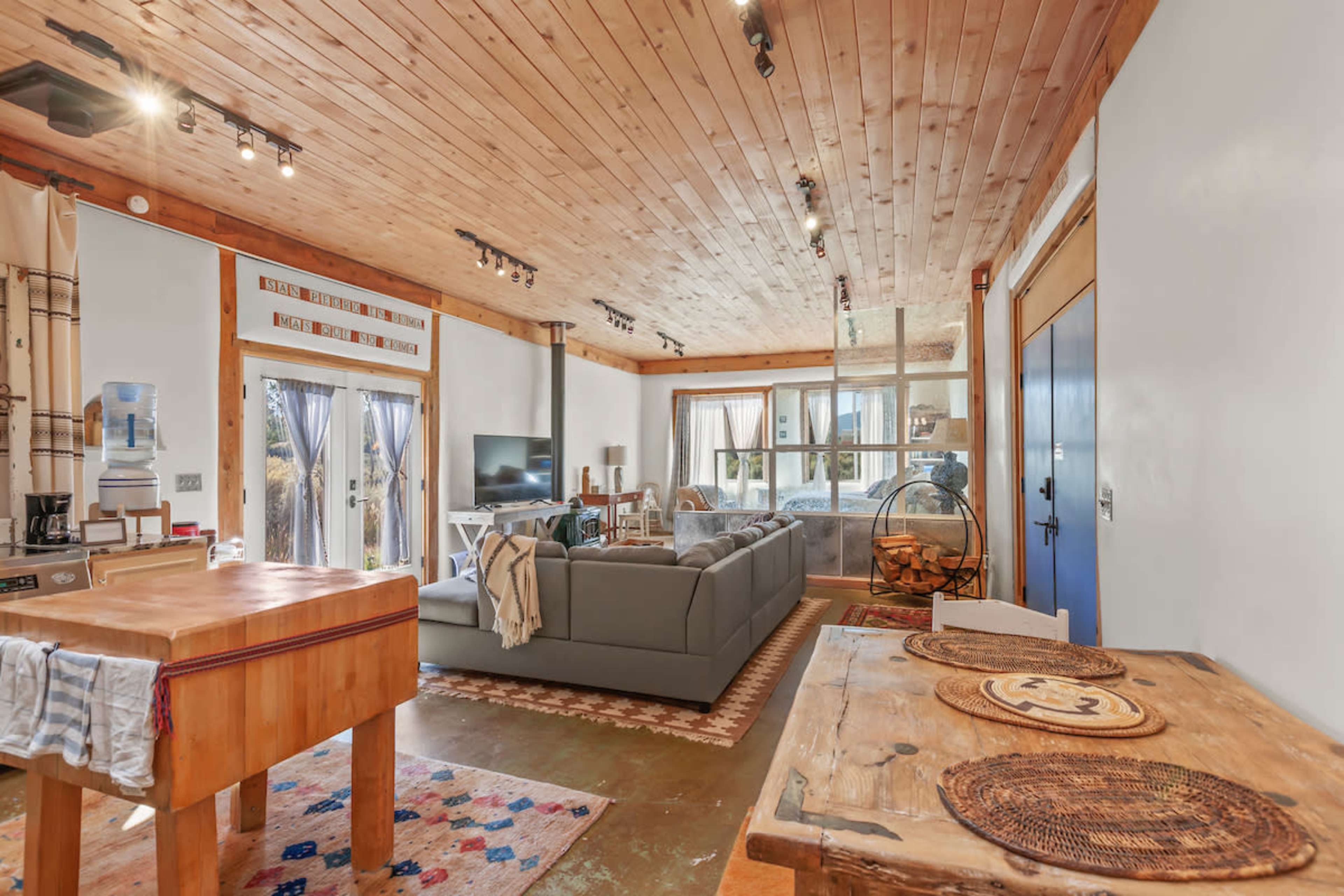 A spacious living area featuring a grey sofa, a wooden dining table, and large windows allowing natural light to fill the room.