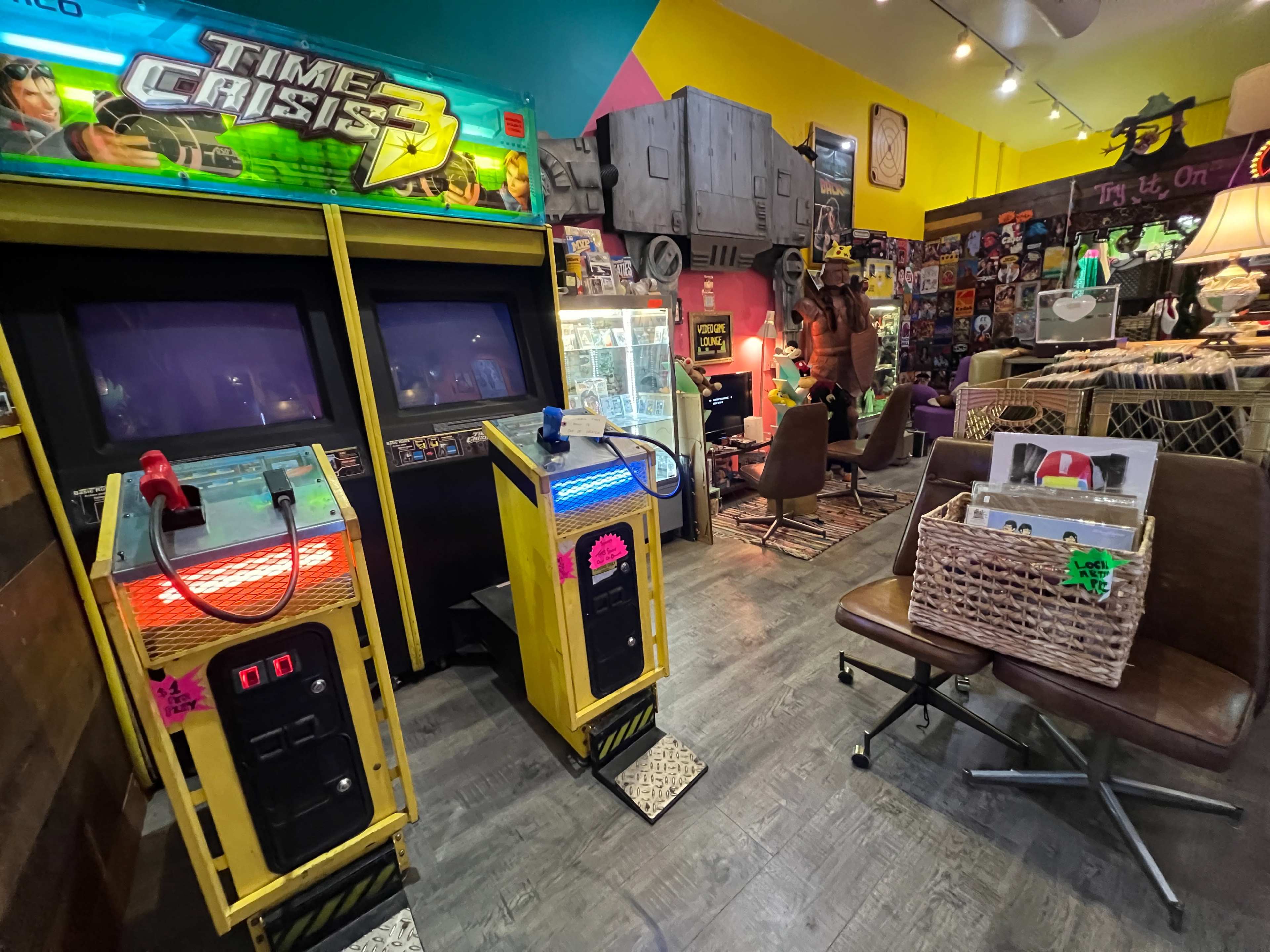 The image shows a colorful arcade room featuring vintage video game machines, retro decor, and seating areas.