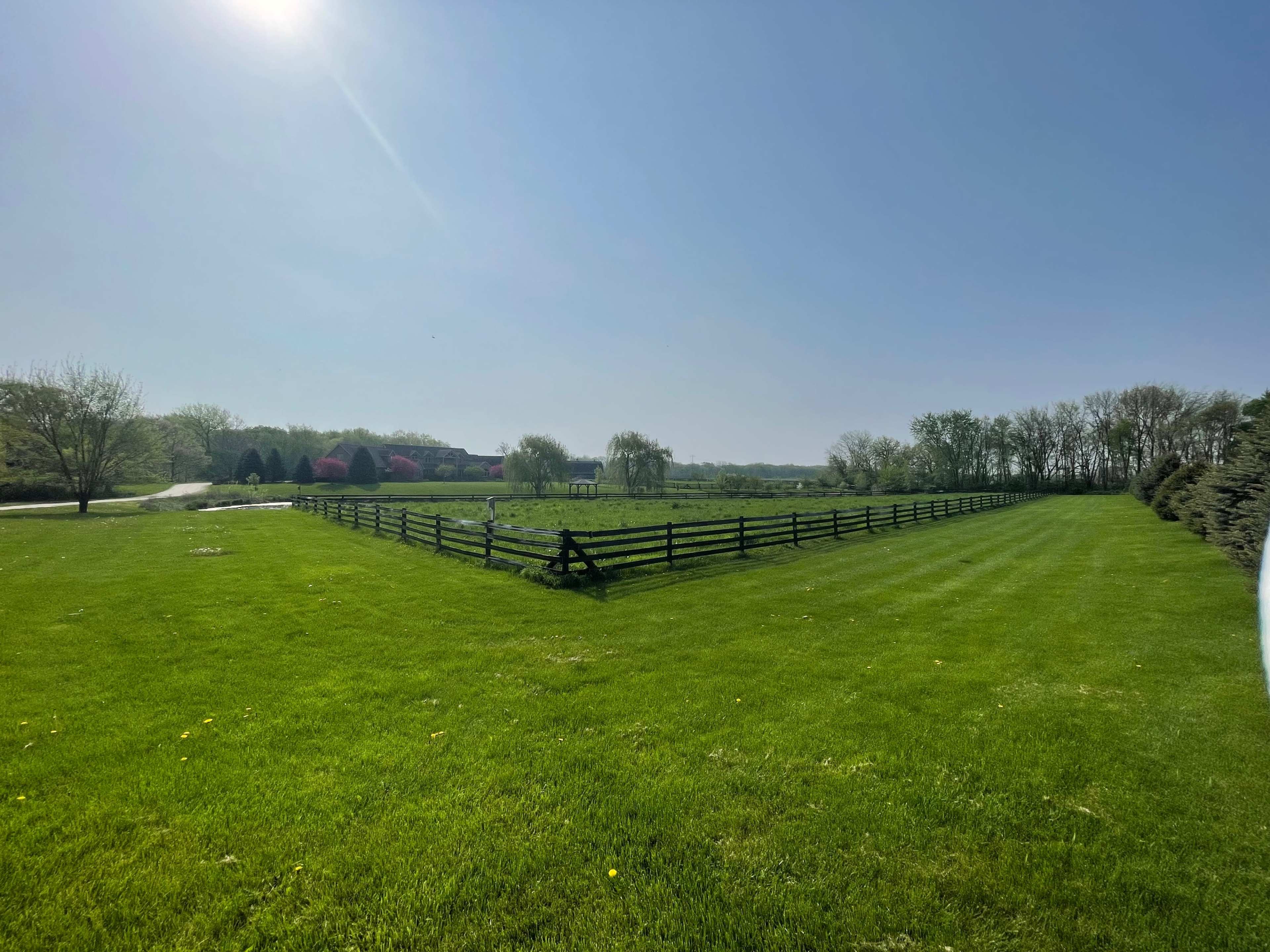 A large green field bordered by a black wooden fence under a clear blue sky.