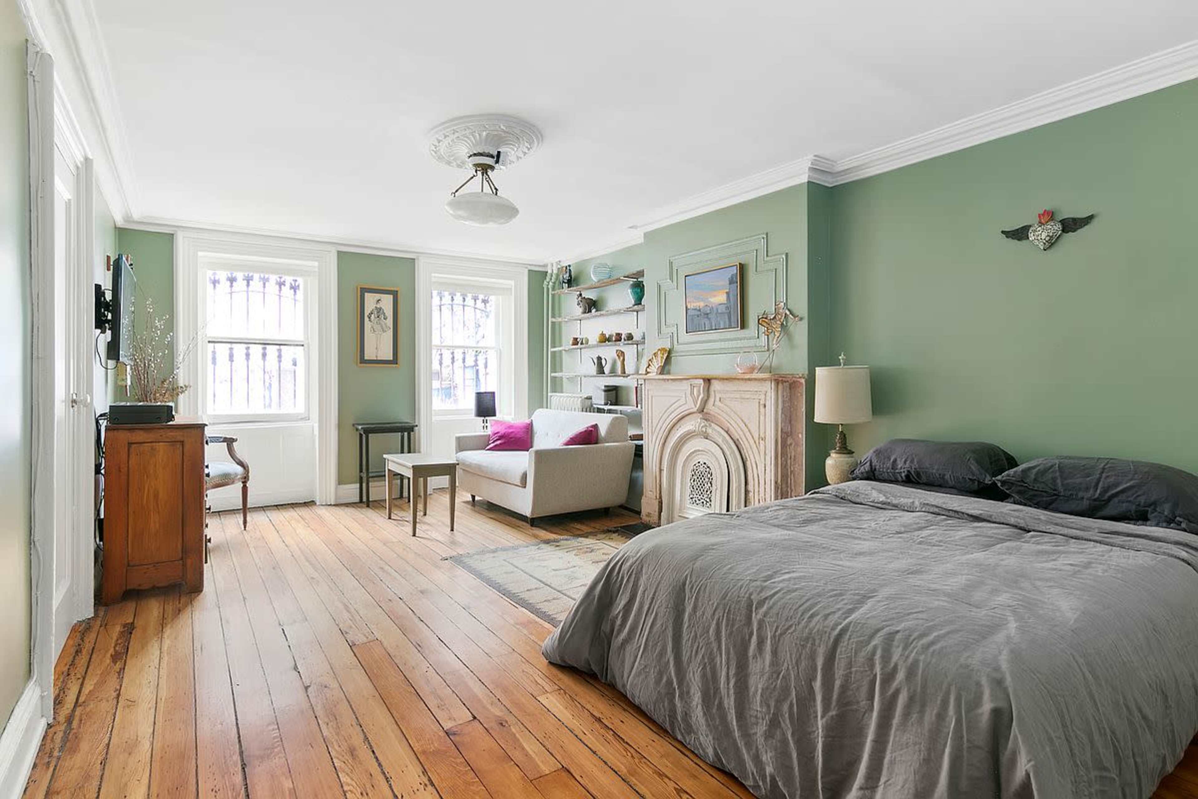 The room features a bed with gray bedding, a wooden floor, a fireplace decoration, and a seating area with a sofa and a small table.