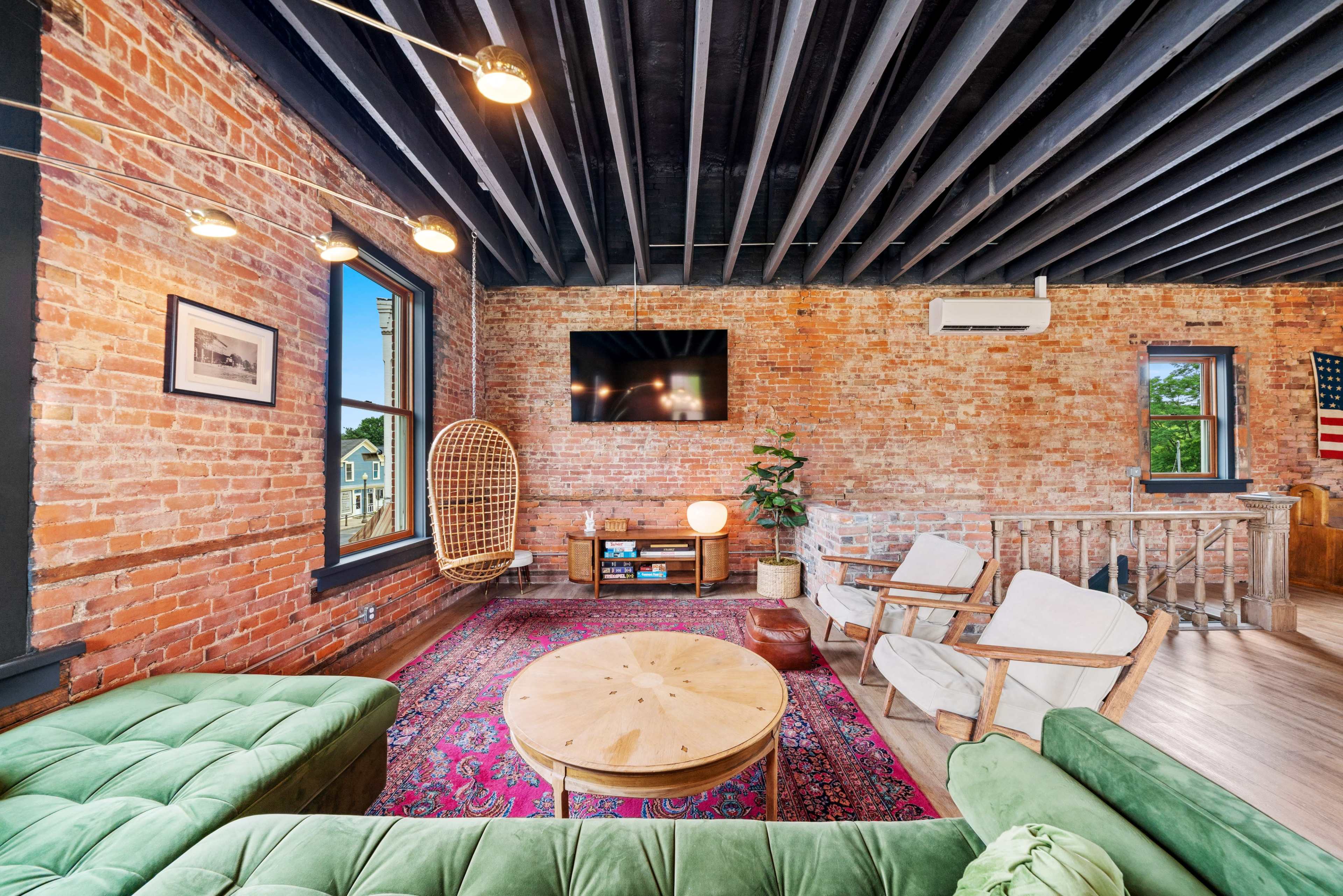 A living room with exposed brick walls, a large green sofa, a round wooden coffee table, and a television mounted on the wall.
