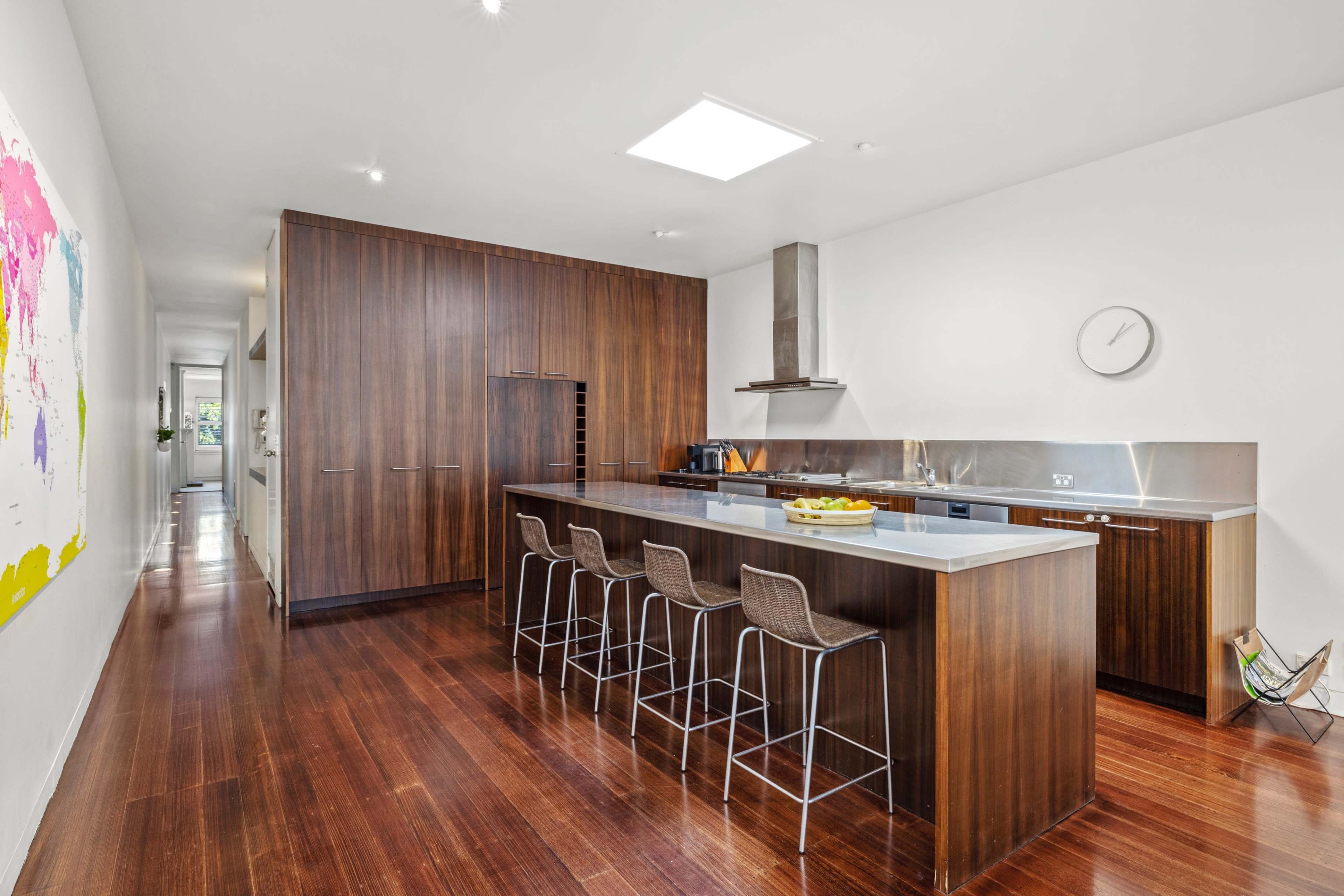 The image shows a modern kitchen featuring dark wooden cabinetry, a central island with bar stools, and sleek stainless steel appliances.
