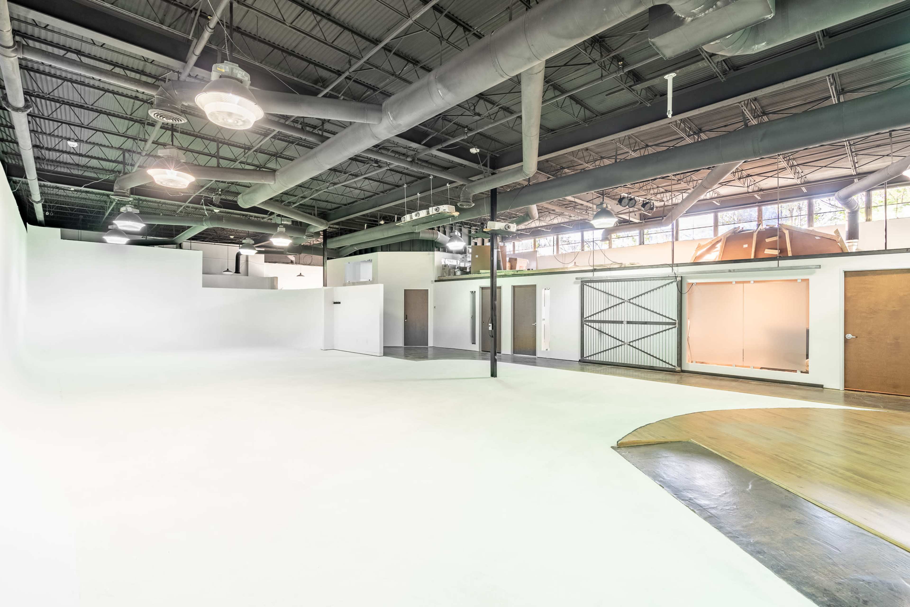 A spacious, empty industrial studio with white walls, polished wooden floors, and large windows.