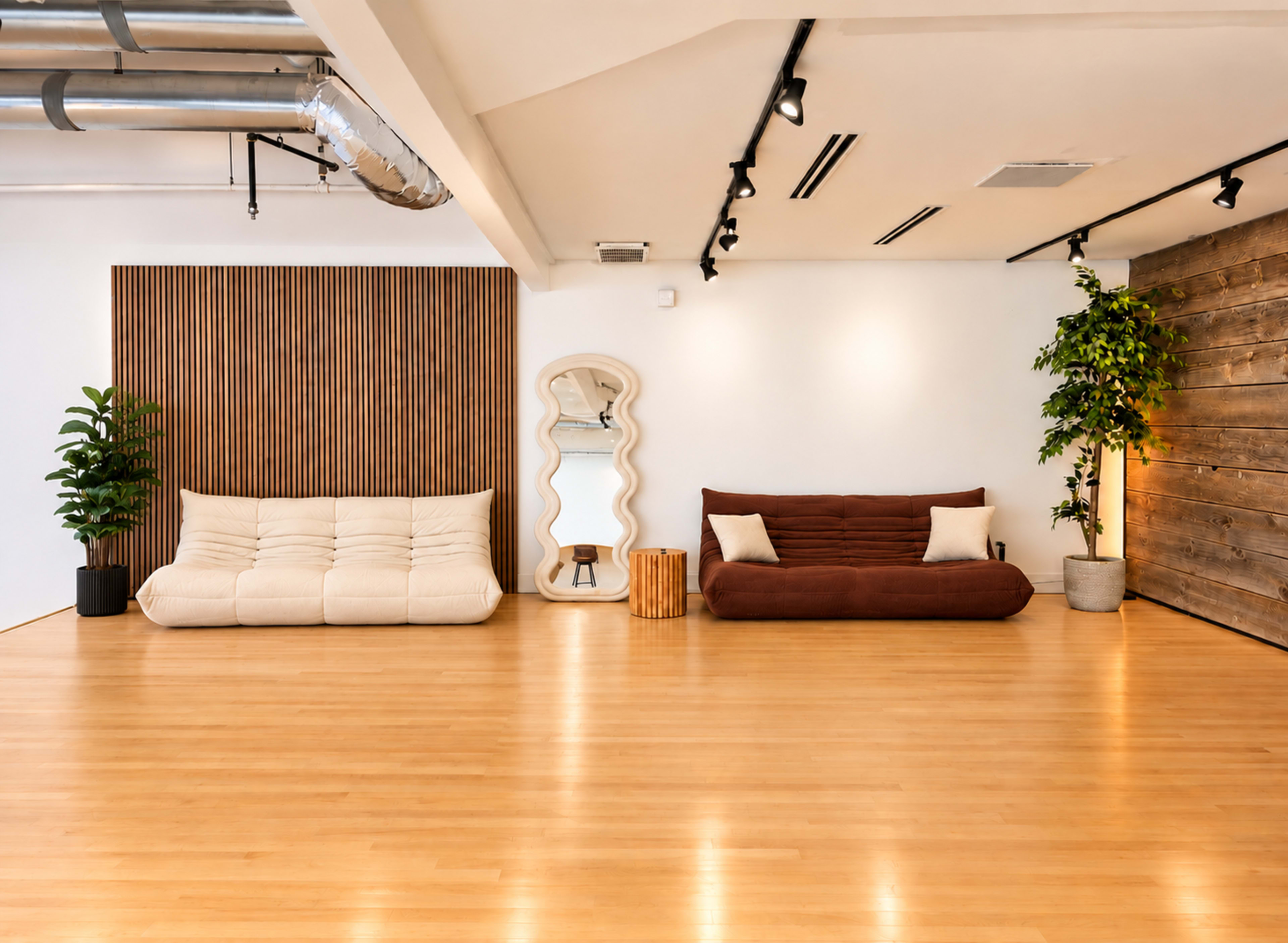 The image shows a spacious, minimalistic living area featuring two sofas, a mirror, a wooden accent wall, and plants on a wooden floor.
