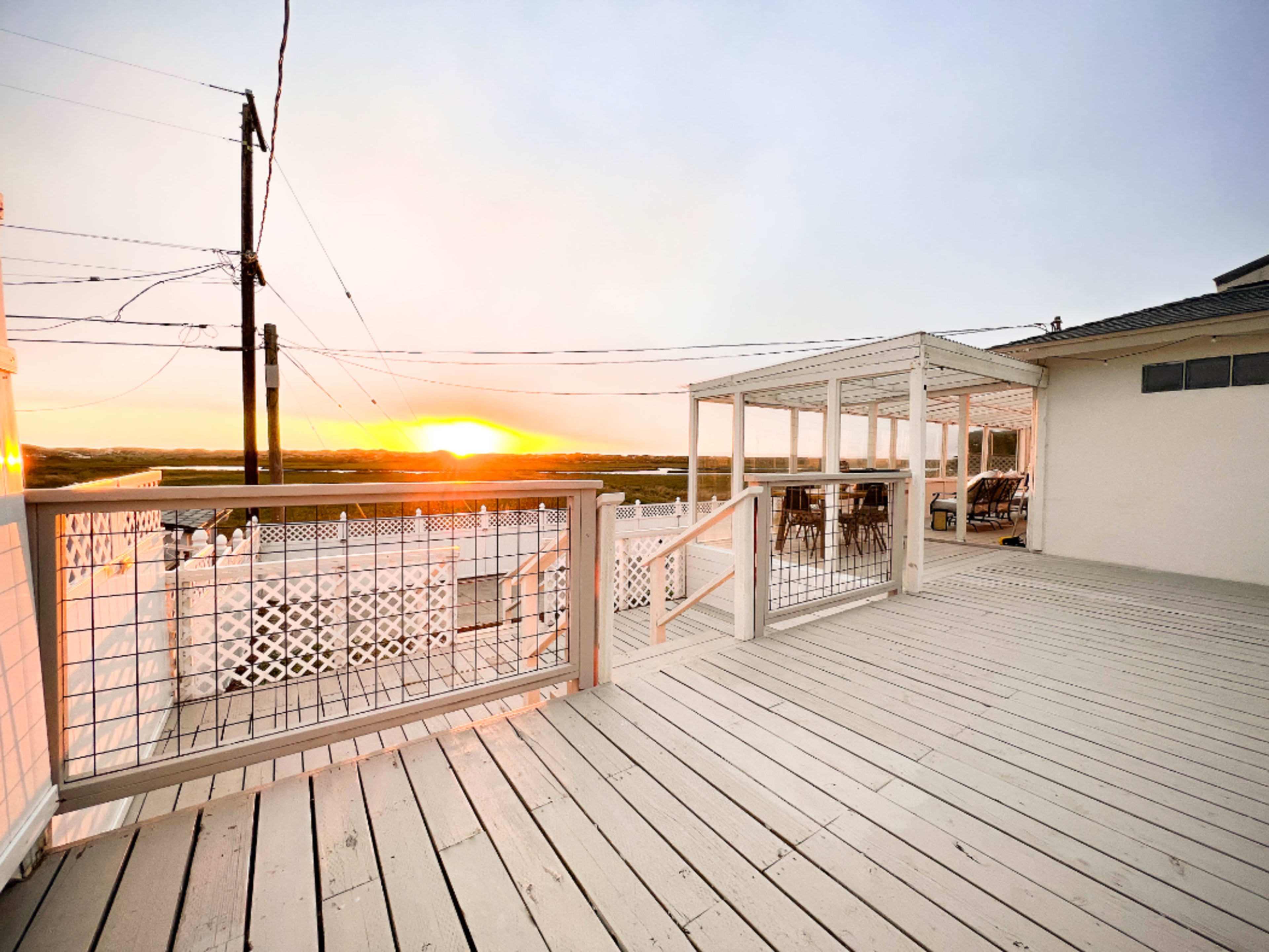 A wooden deck overlooking a sunset with power lines in the background.