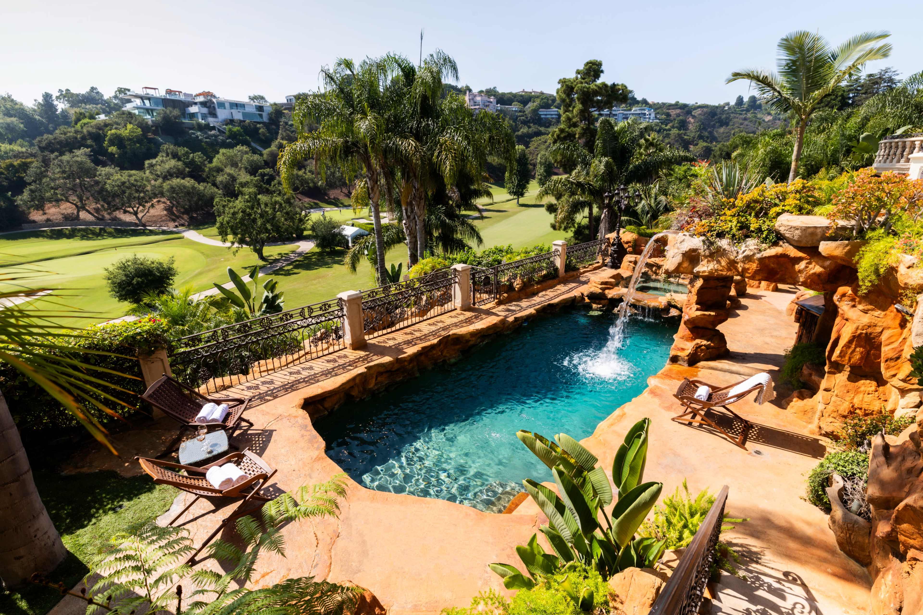 A luxurious pool surrounded by tropical plants and a view of a golf course in the background.