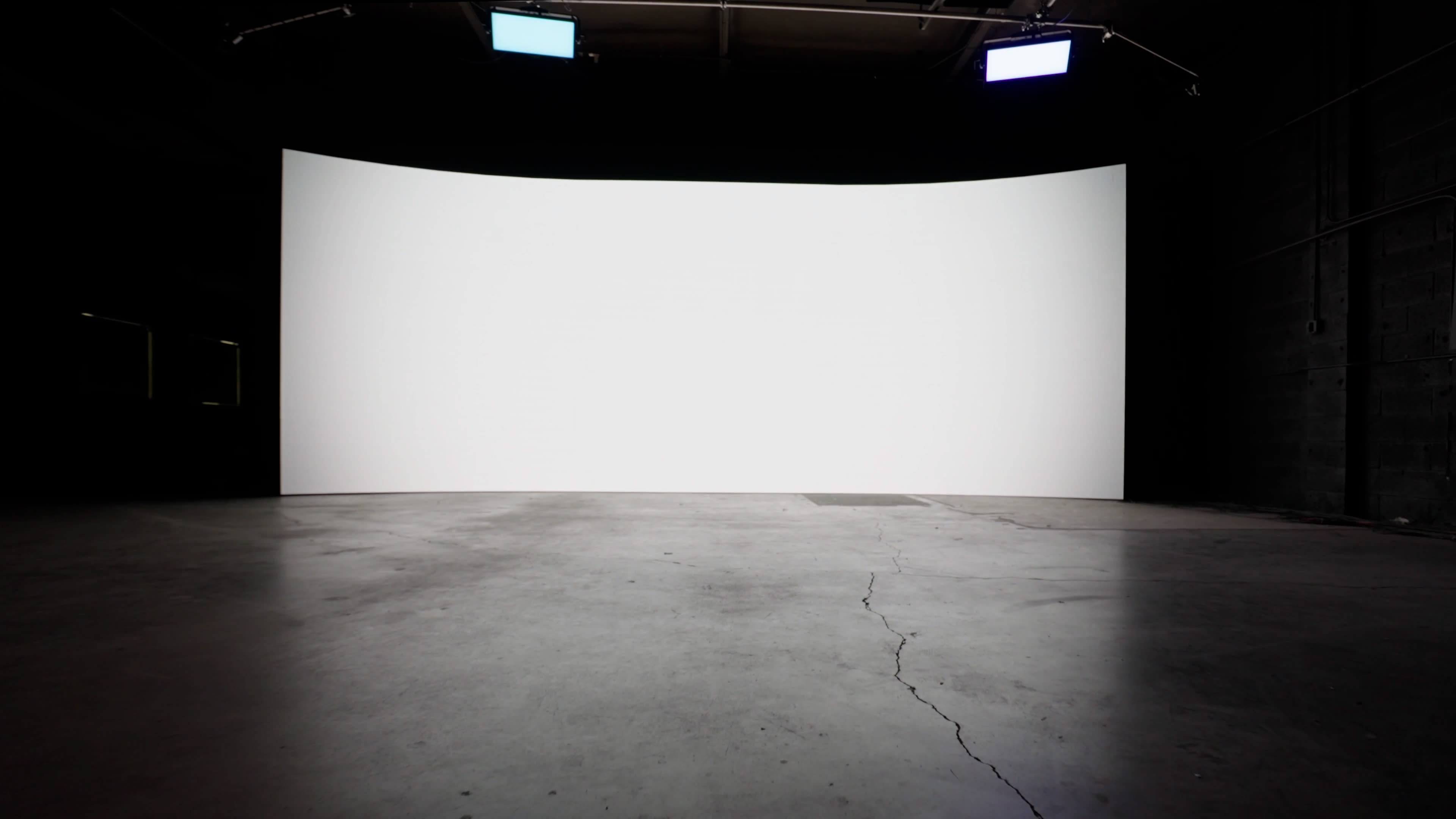 A large, empty studio space with a curved white backdrop and concrete flooring.