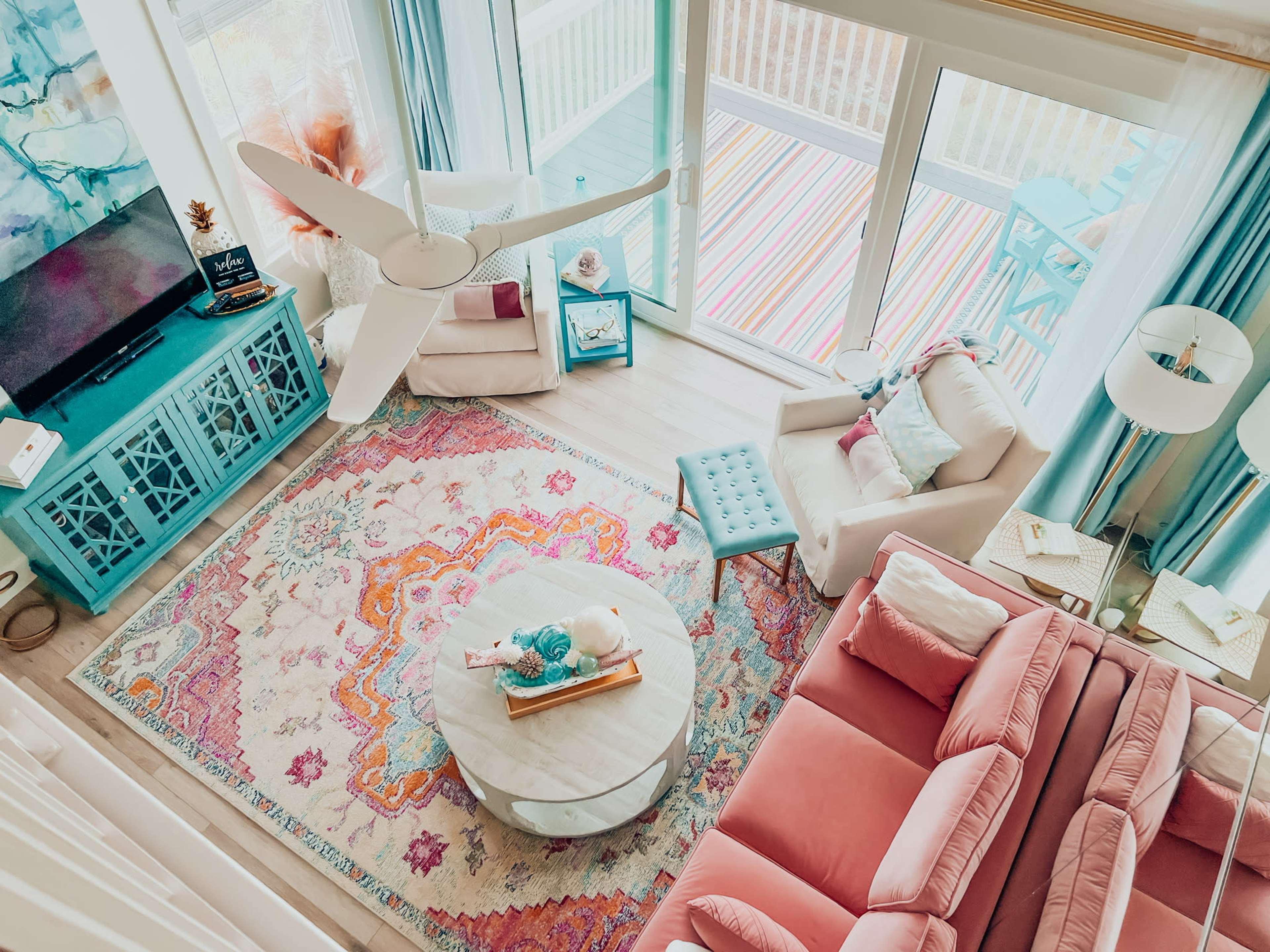 A brightly decorated living room with a round coffee table, pastel-colored seating, and large windows allowing natural light to fill the space.
