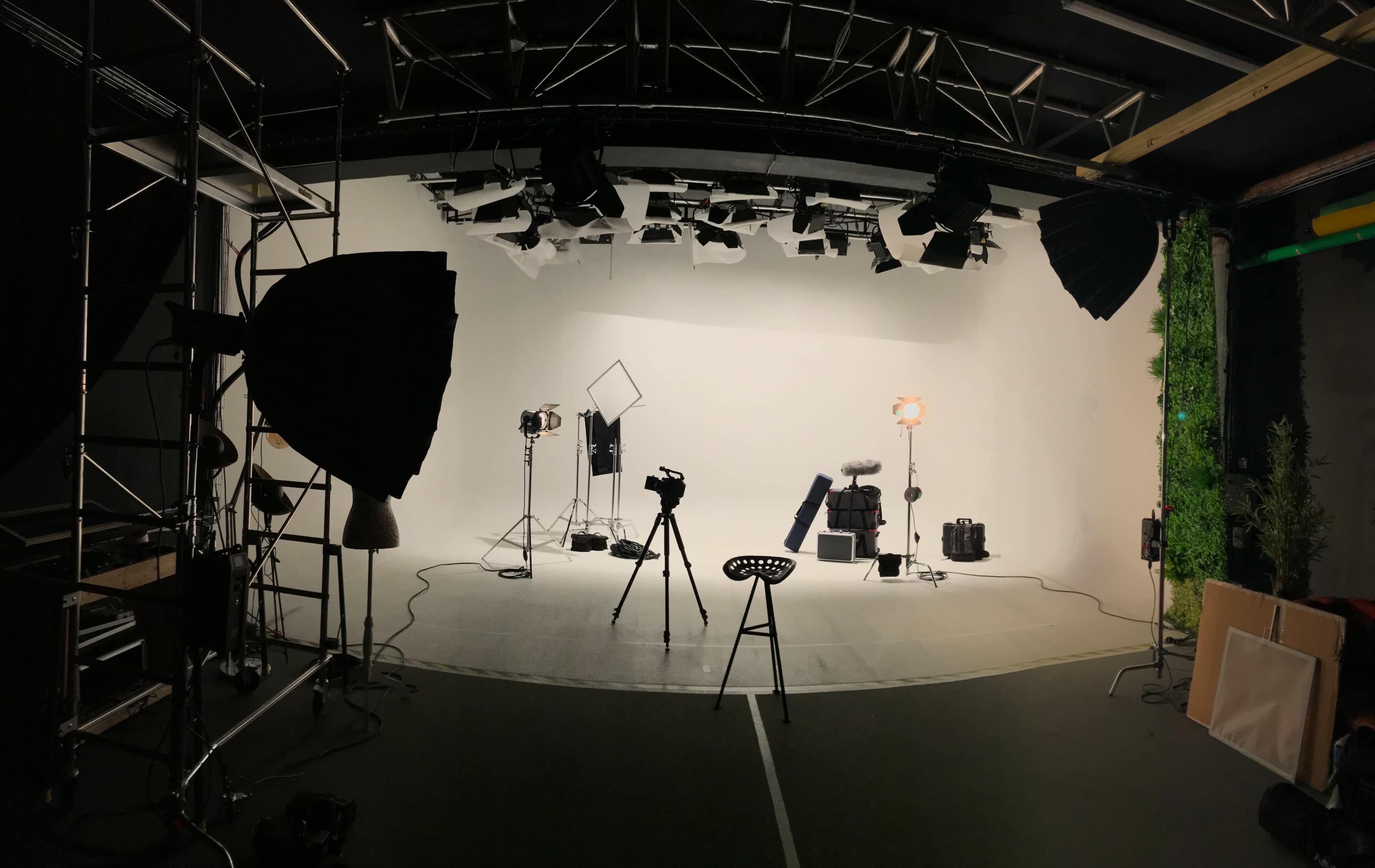 The image shows a photography studio setup with various light sources, cameras, and equipment arranged on a stage with a white backdrop.