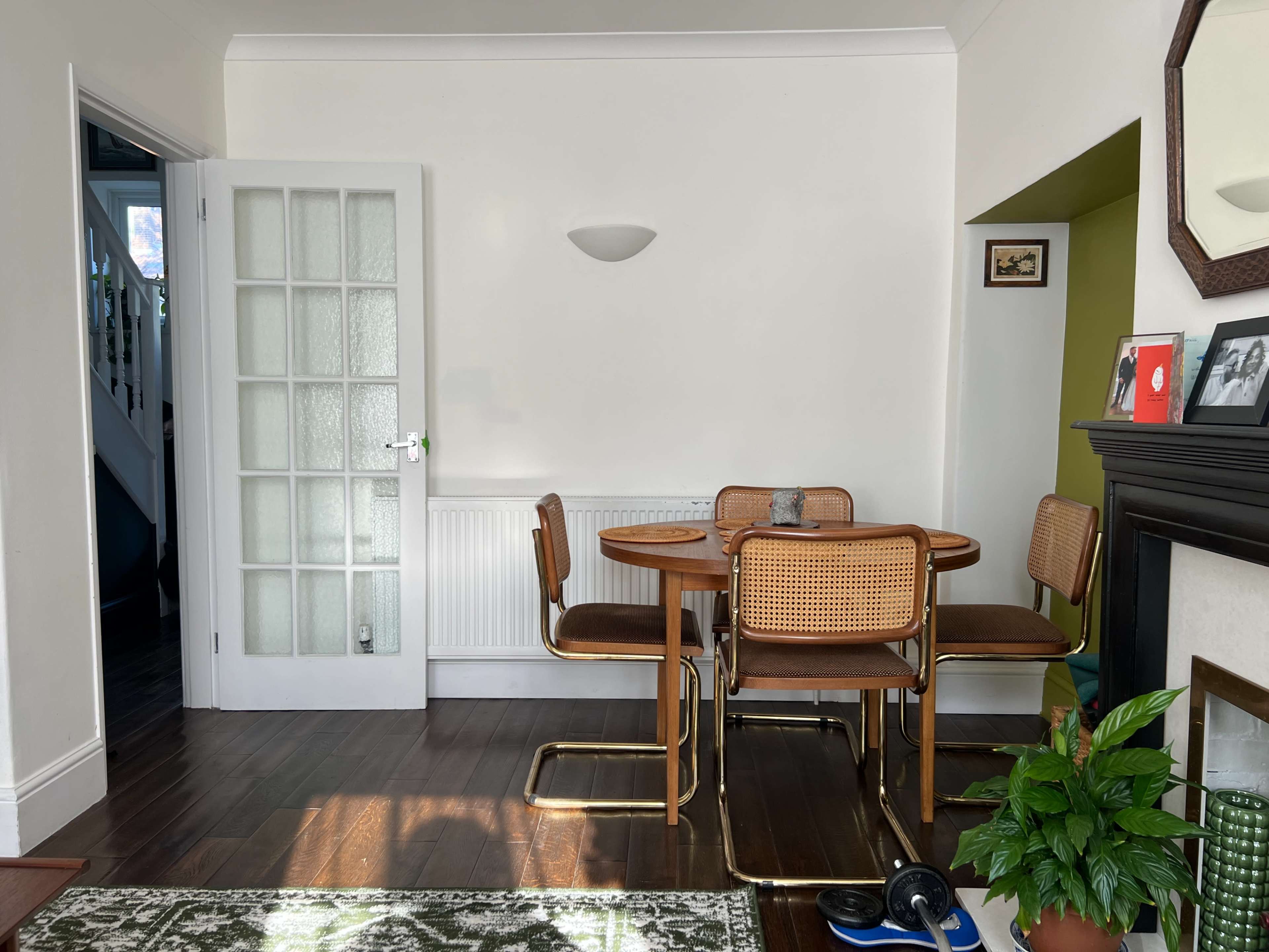 A dining area features a round table with four chairs, a plant in the corner, and a doorway leading to another room.