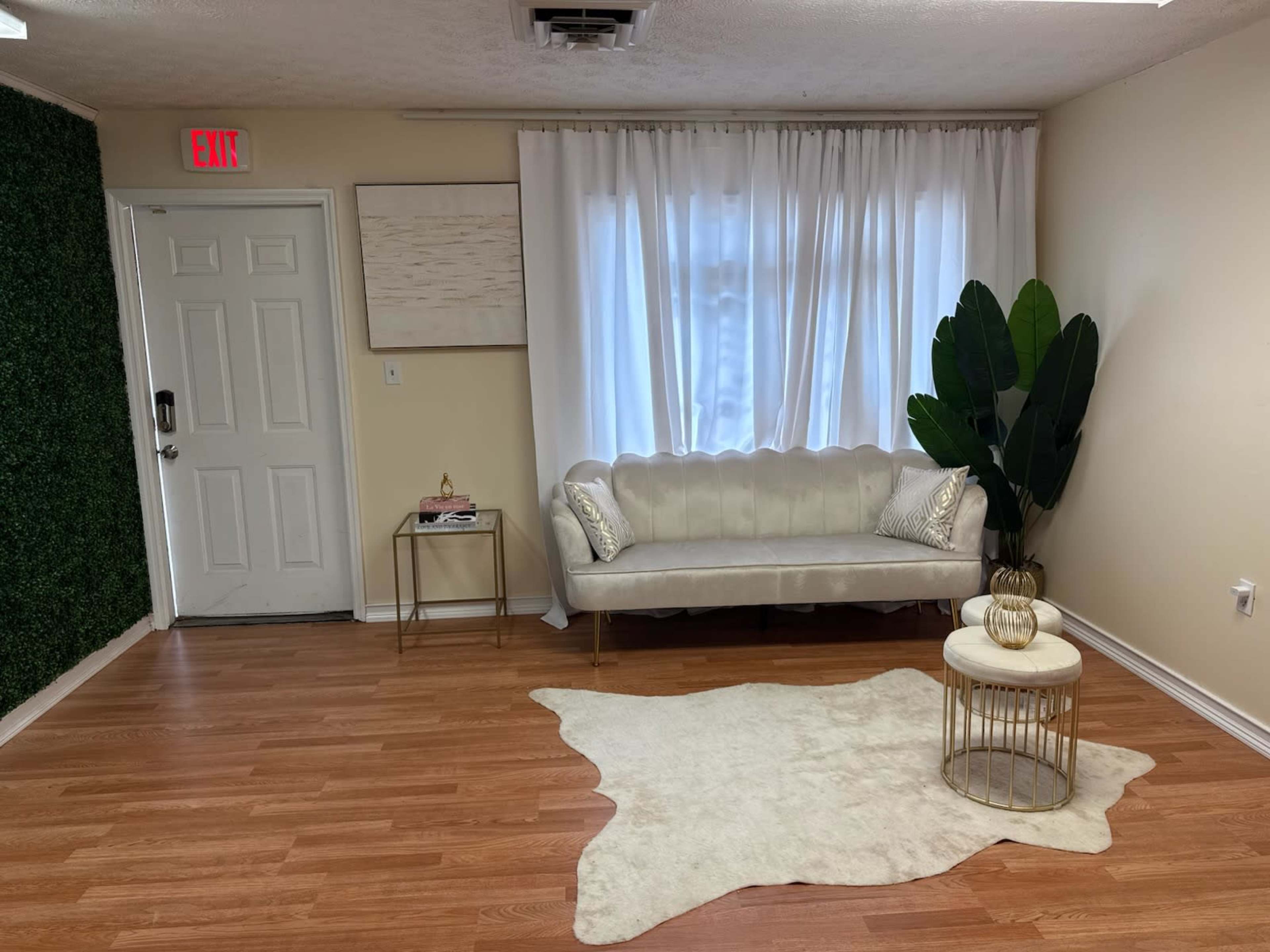 The image shows a cozy room featuring a light-colored couch, a decorative rug, a coffee table, and a potted plant, with one wall covered in greenery.
