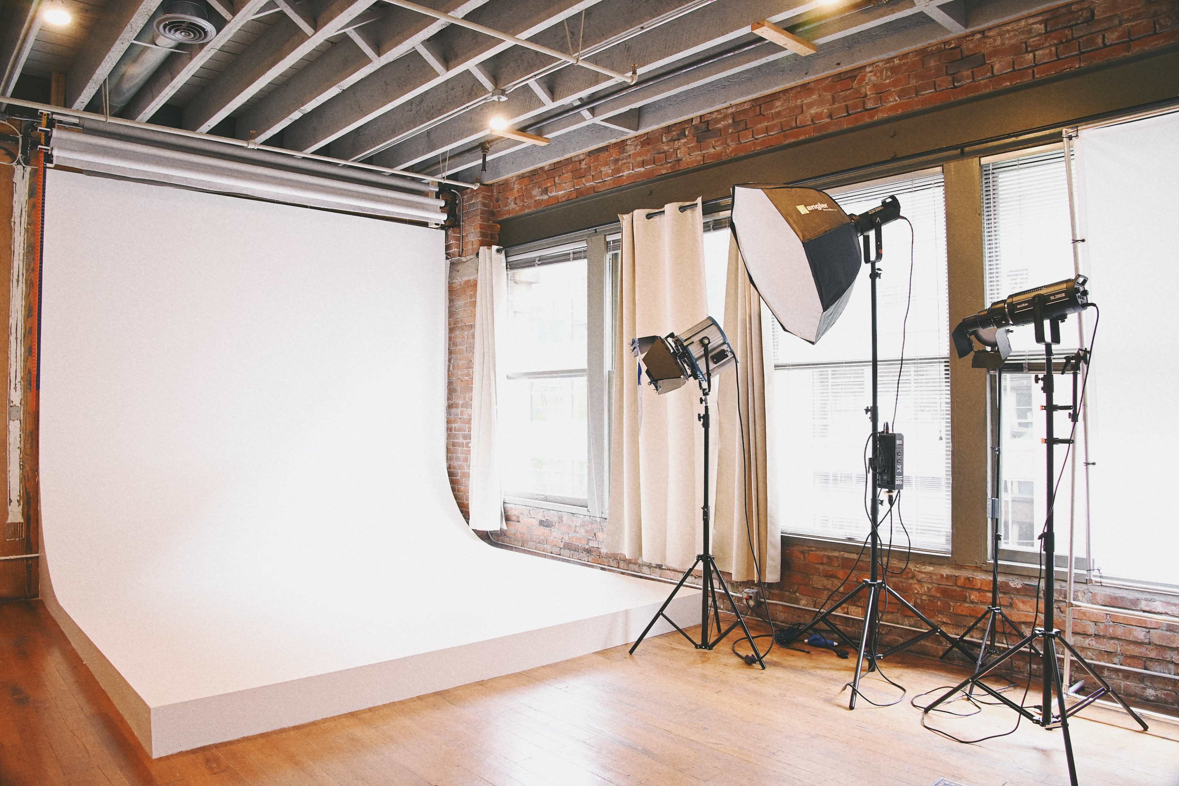 The image shows a photography studio with a seamless white backdrop, lighting equipment, and large windows allowing natural light.