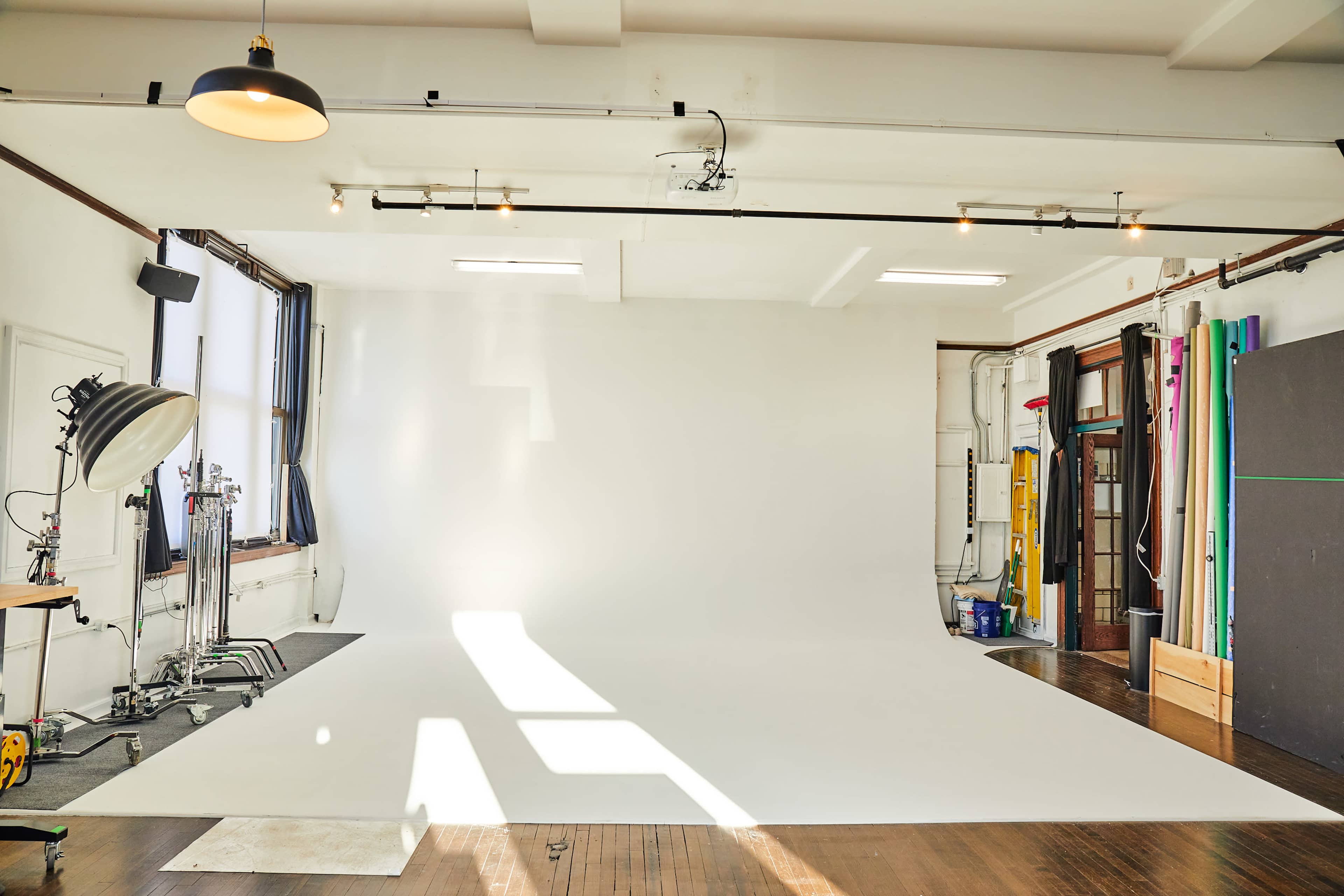 A bright photography studio with a large white backdrop, natural light coming through the windows, and various equipment set up along the walls.