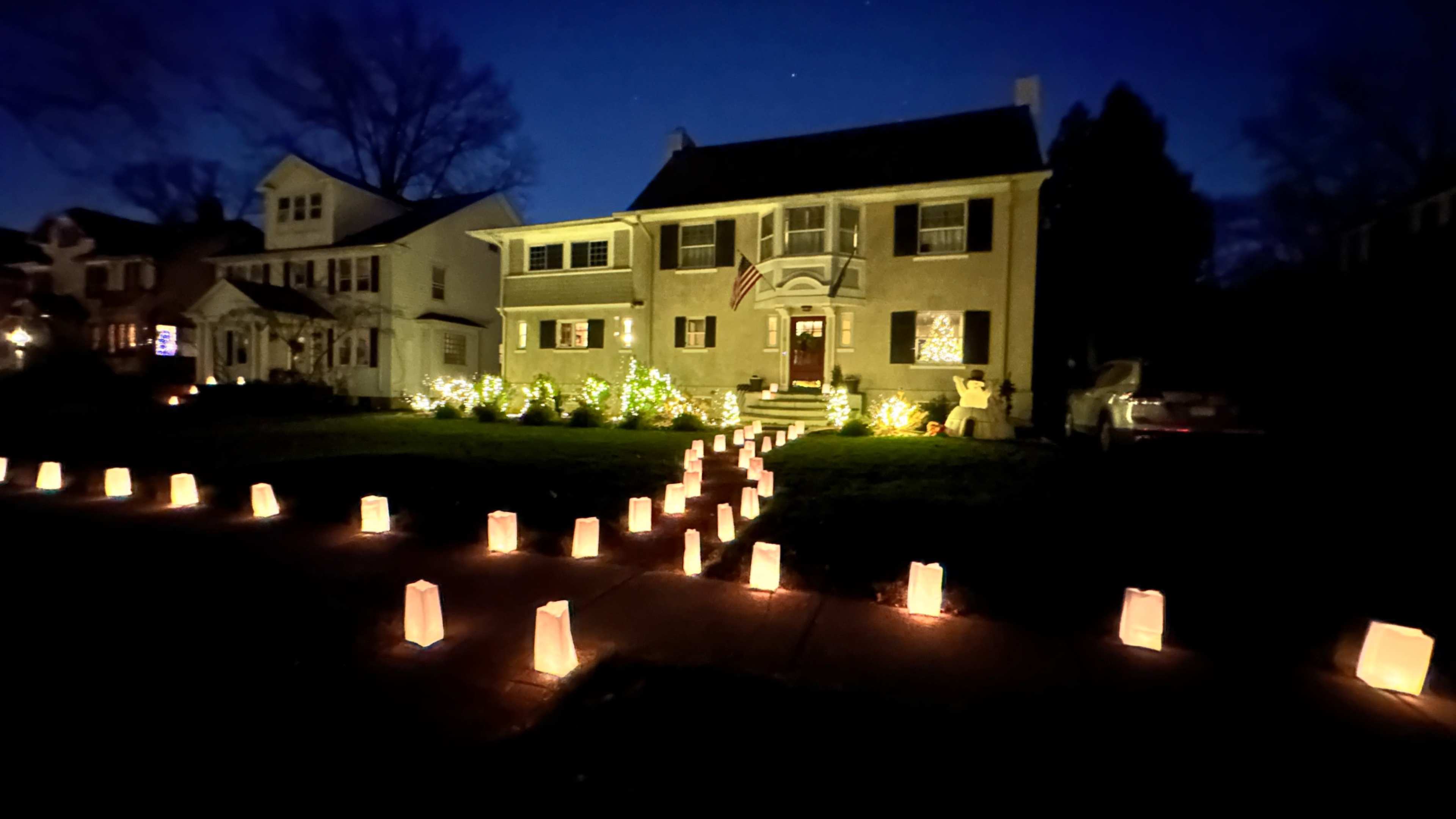 A well-lit house with festive decorations and a pathway of glowing luminaries leading up to the front door.