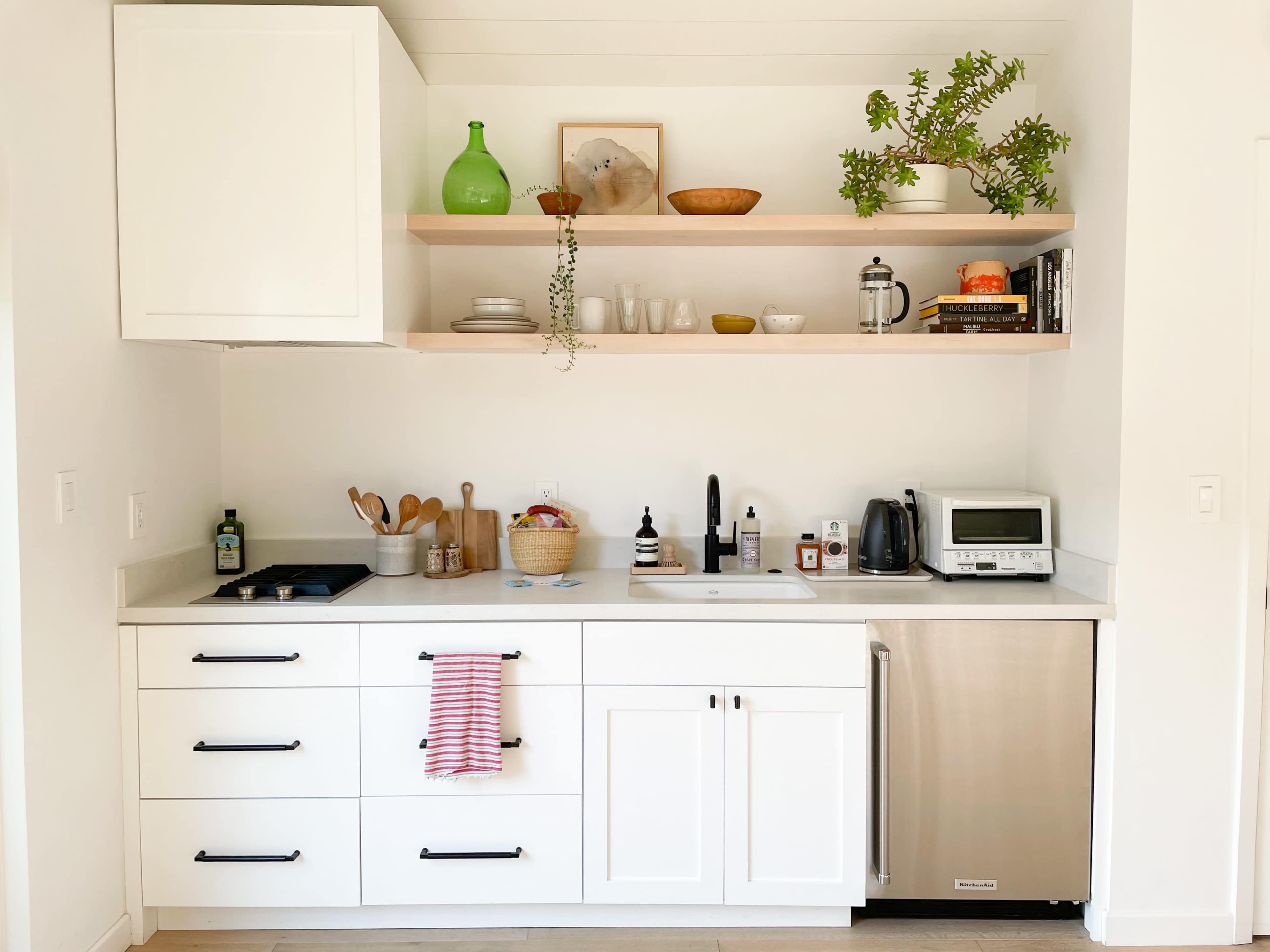 A modern kitchen features white cabinets, open shelves with various kitchen items, and stainless steel appliances.