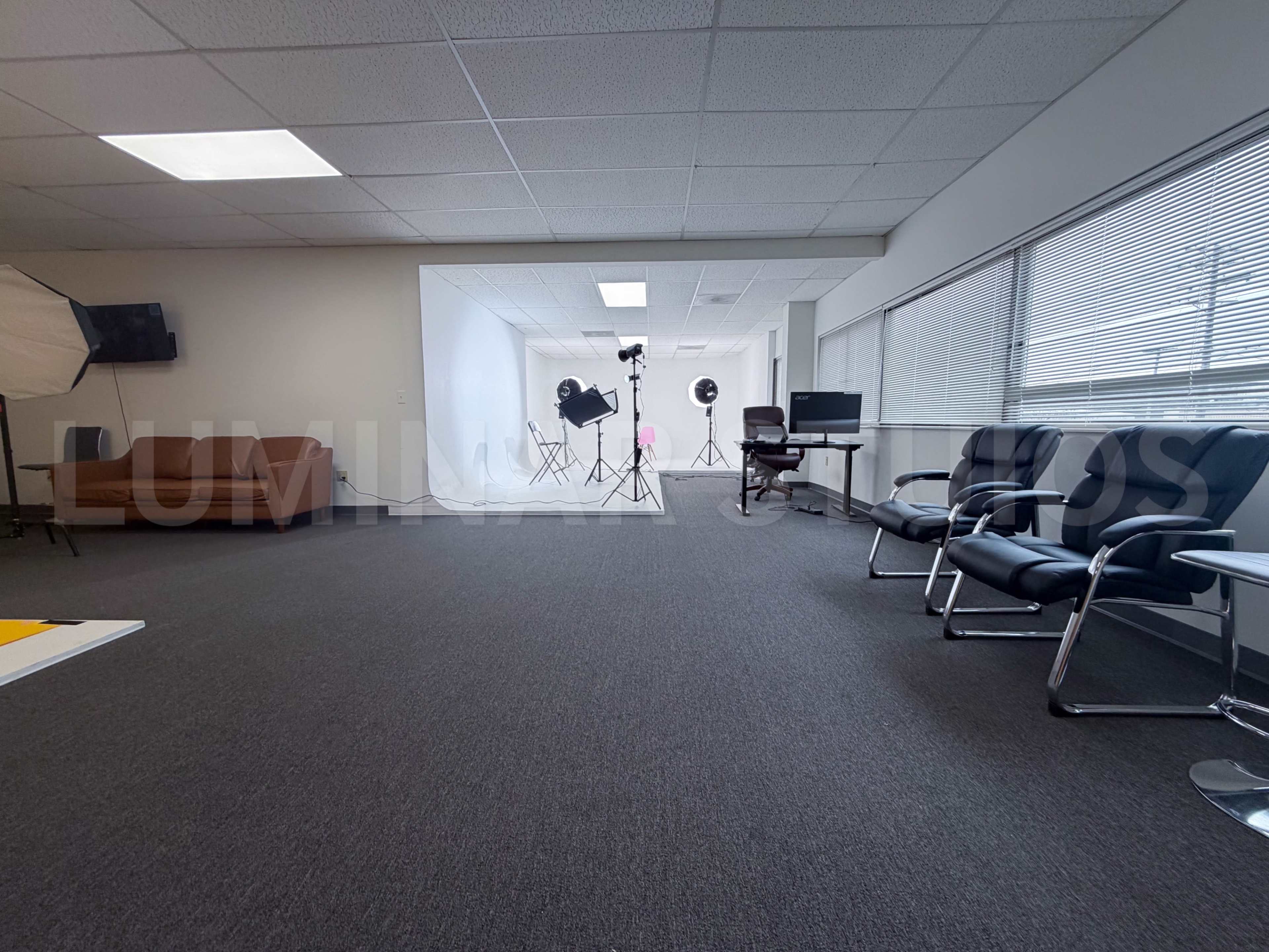 The image depicts a spacious, well-lit studio equipped with photography lighting, a computer workstation, and modern seating arrangements.