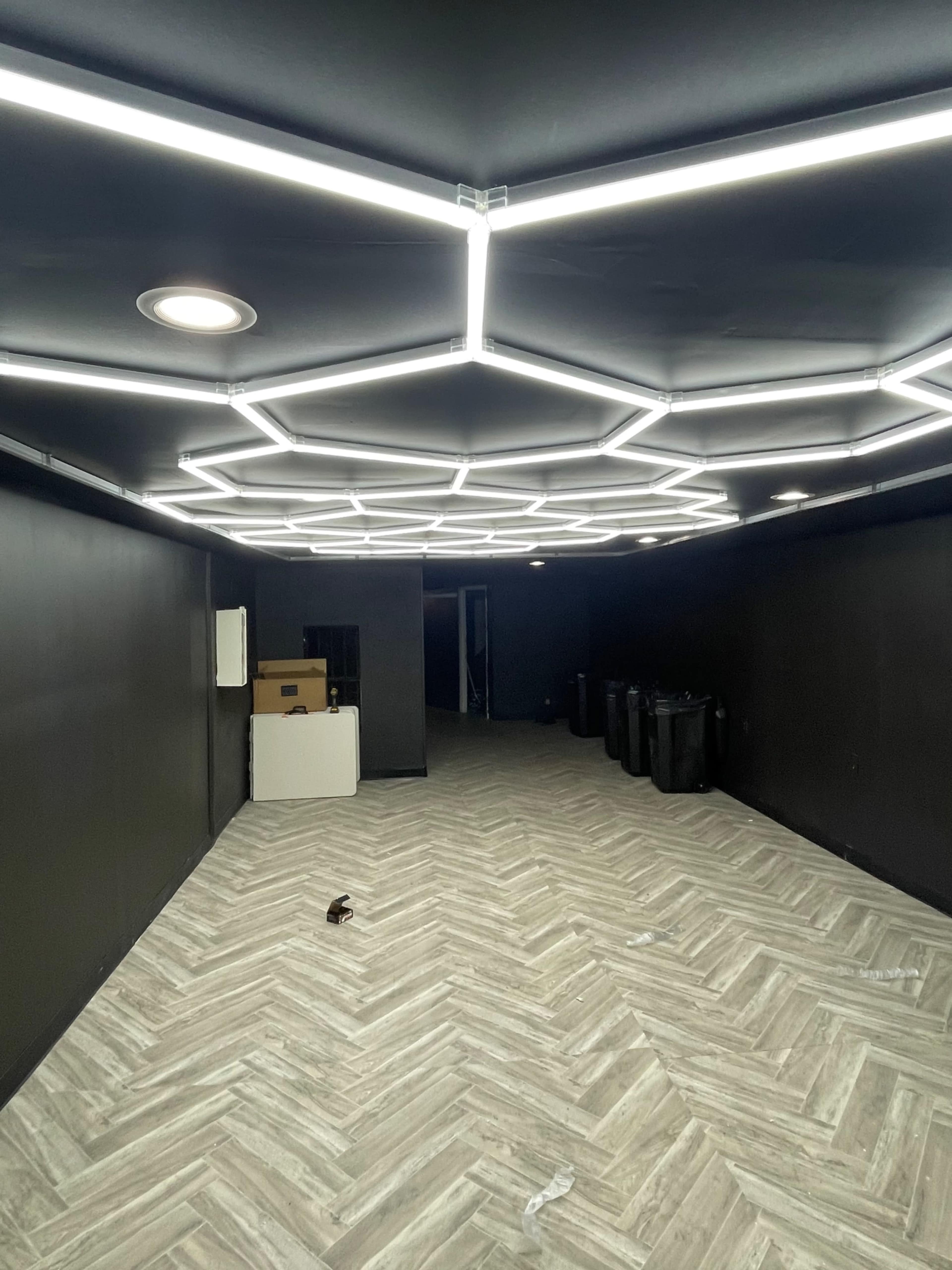 A spacious, dimly lit room with a geometric, illuminated ceiling and a herringbone-patterned floor.