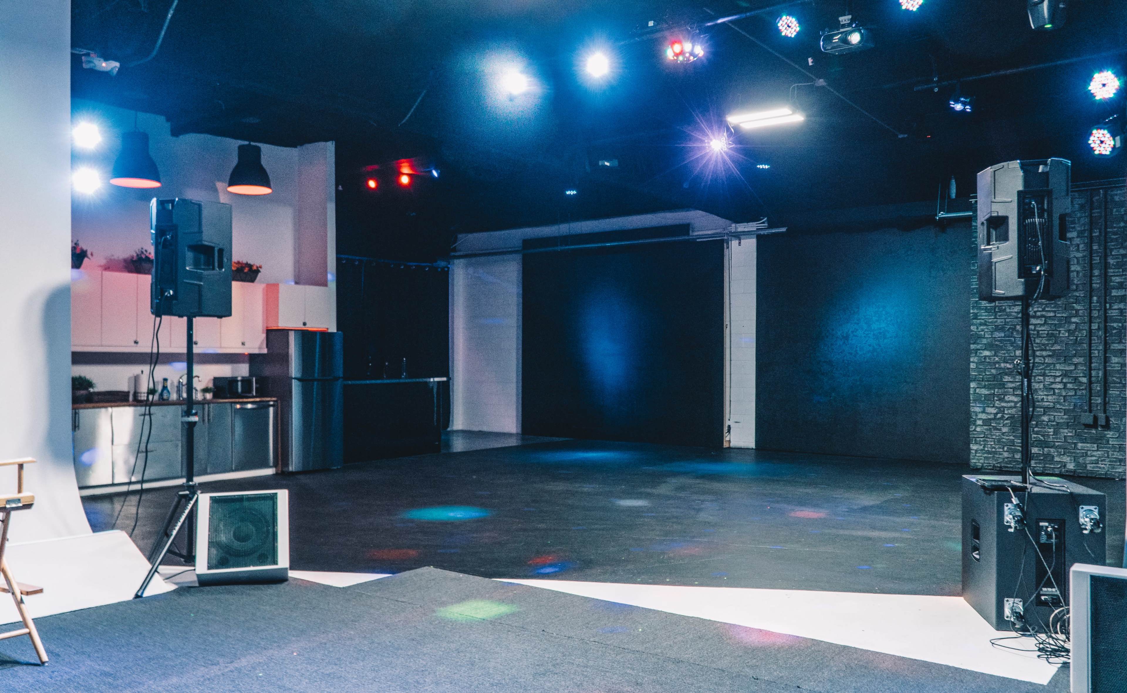A spacious studio with dark flooring, a minimalist kitchen area, and several lights illuminating the room.
