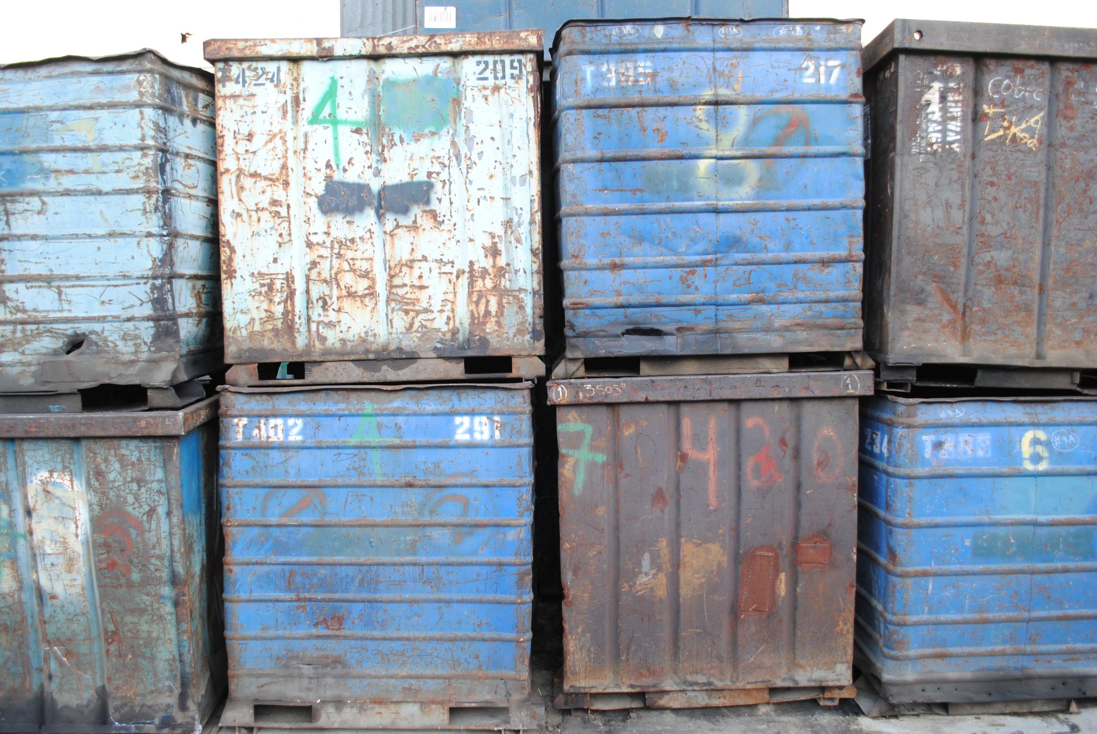 Several blue metal storage containers are stacked on top of each other, showing signs of wear and graffiti.