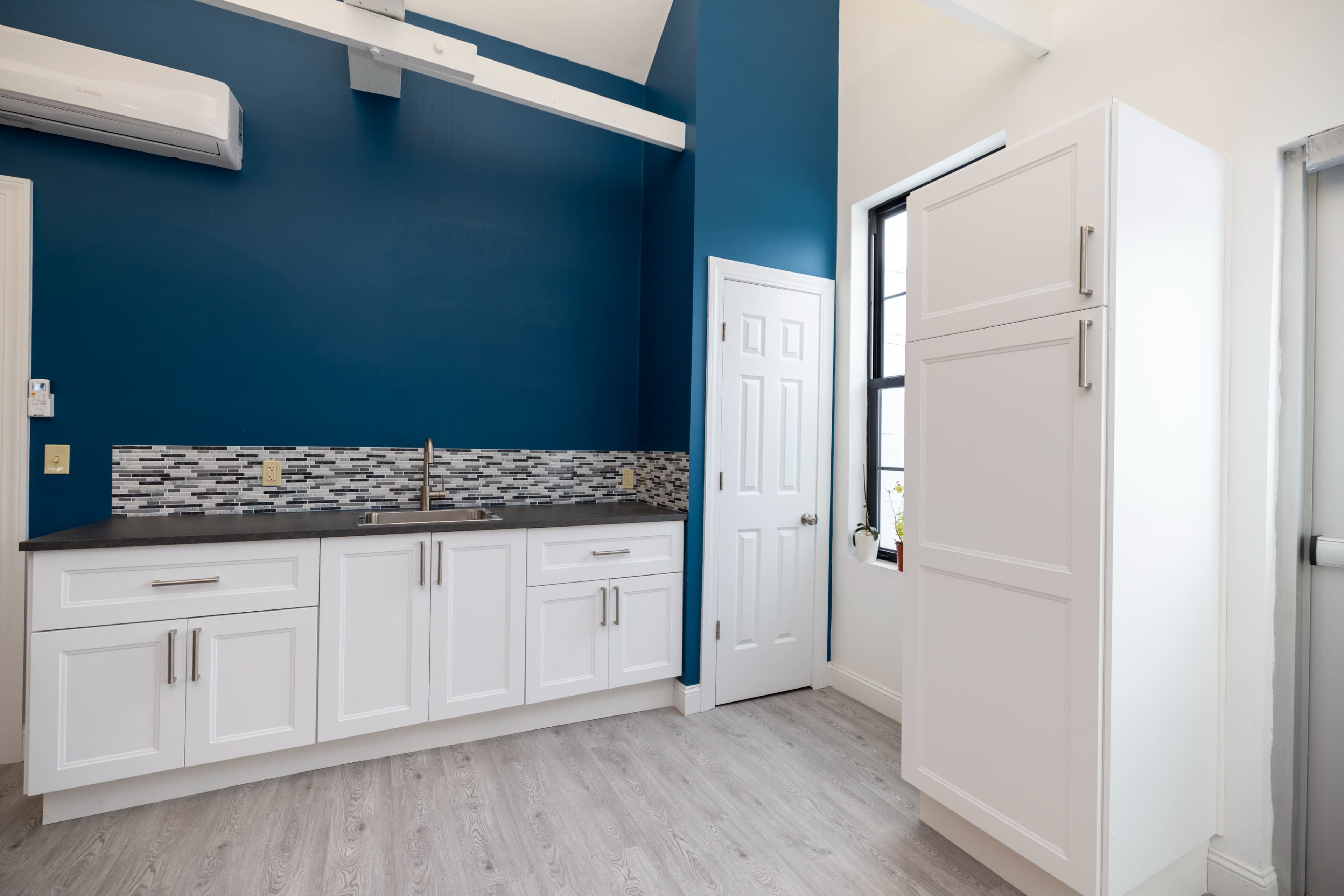 A kitchen with white cabinetry, a dark countertop, and a blue accent wall, featuring a stainless steel backsplash and a large white refrigerator.
