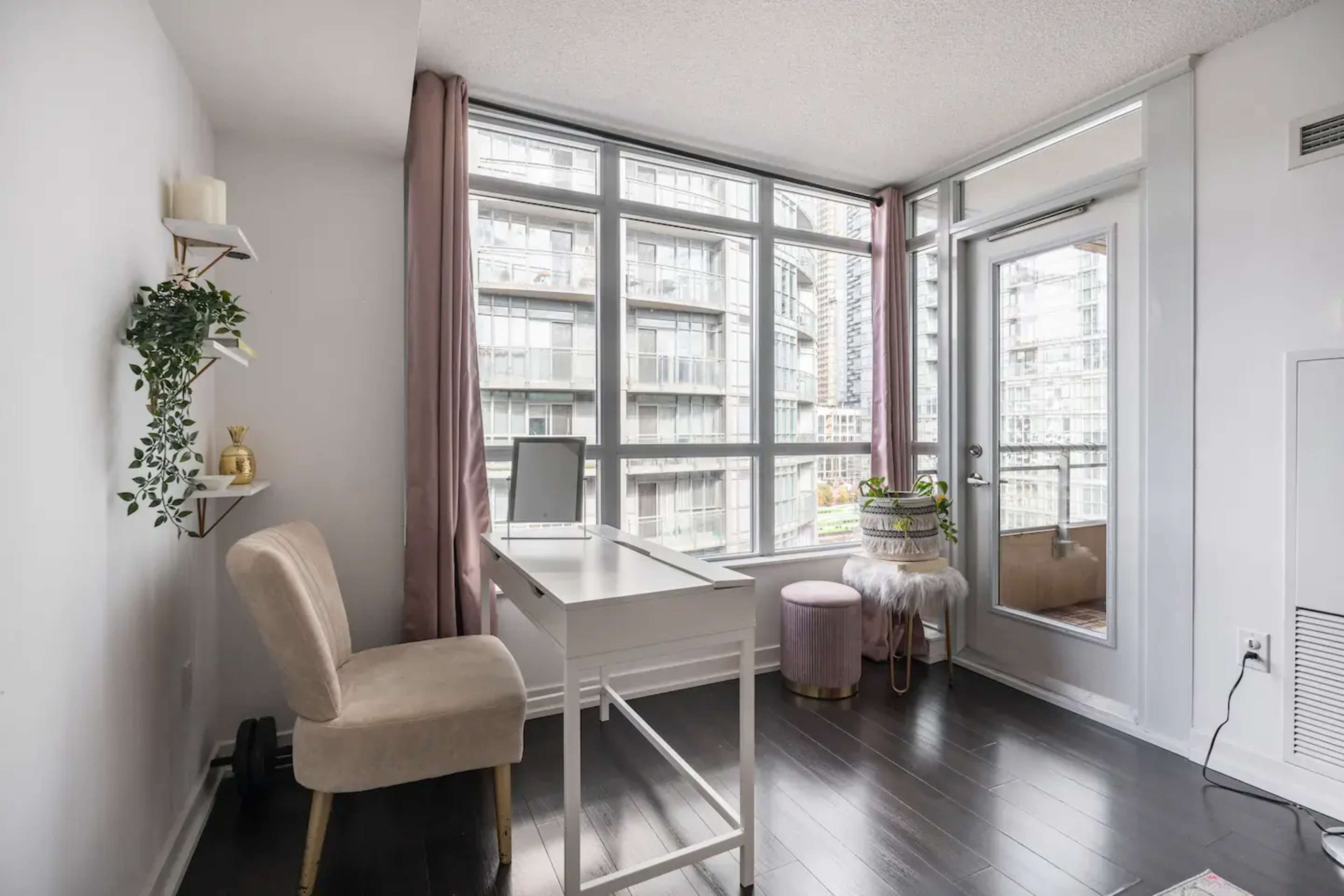 A small office space features a white desk, a chair, and large windows overlooking an urban view.