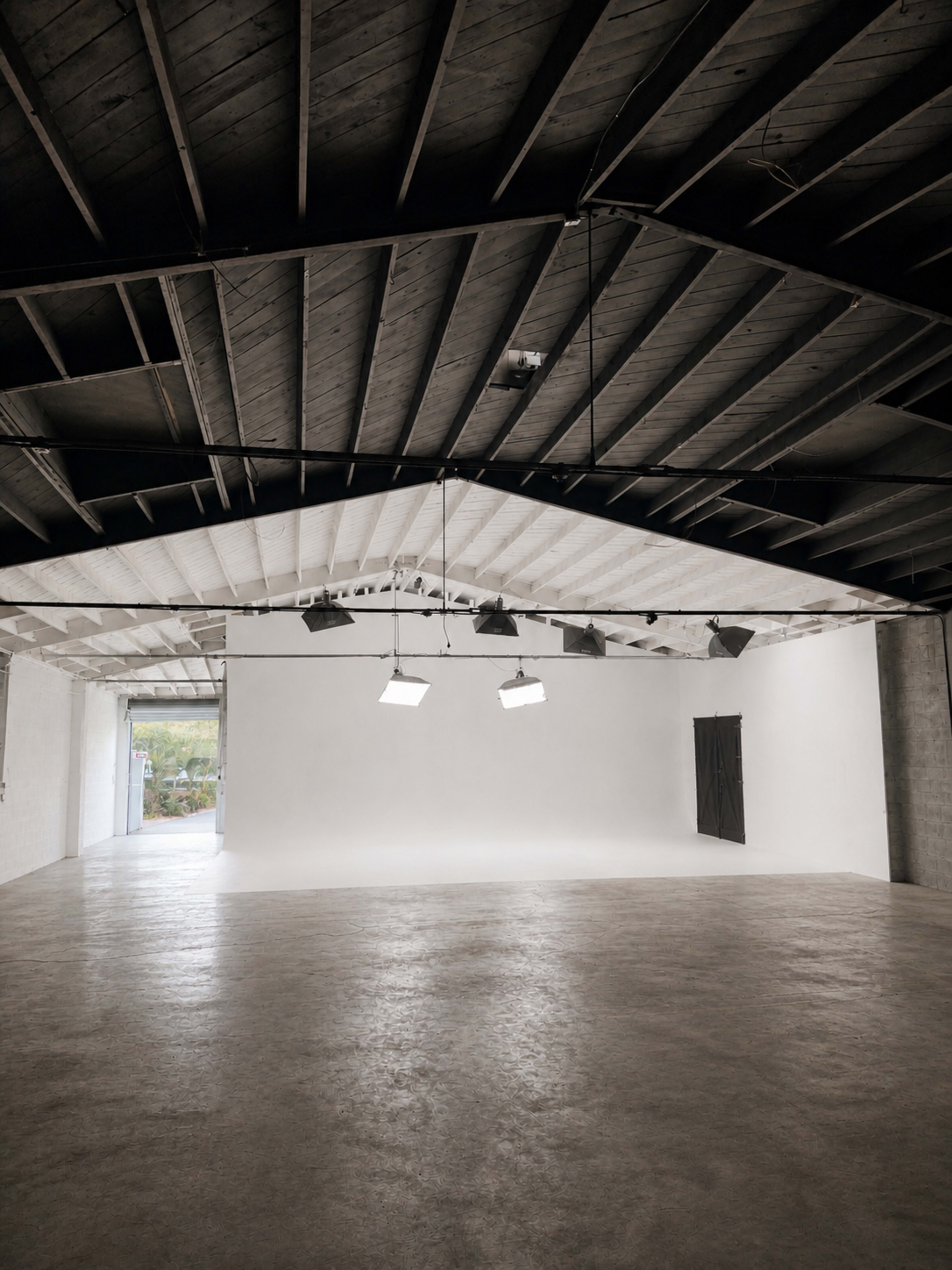 The image shows a spacious, well-lit studio with a high ceiling and large white walls, featuring two lights suspended from the roof.