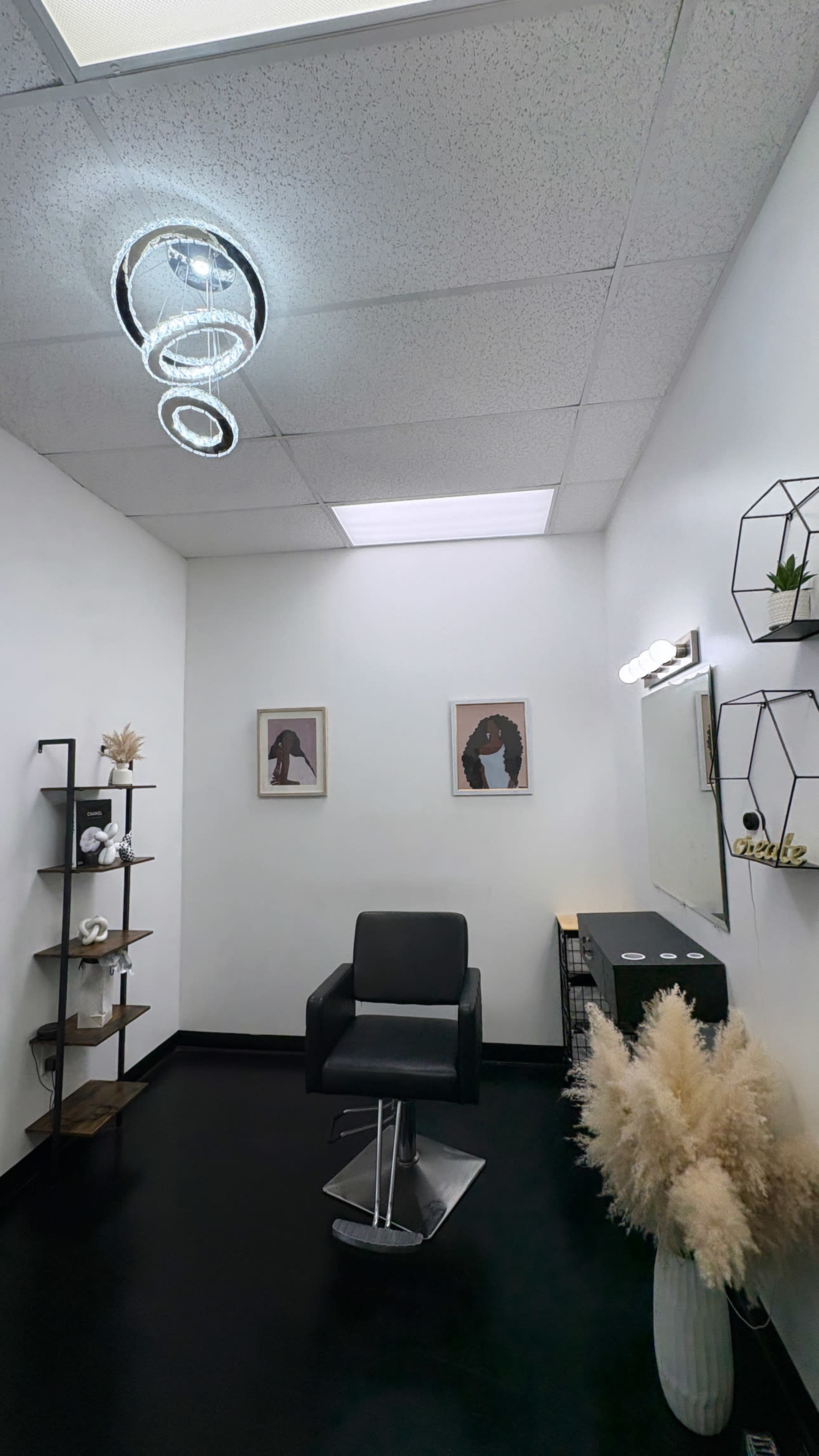 The image shows a modern hair salon interior featuring a black styling chair, decorative wall art, and minimalist shelving.