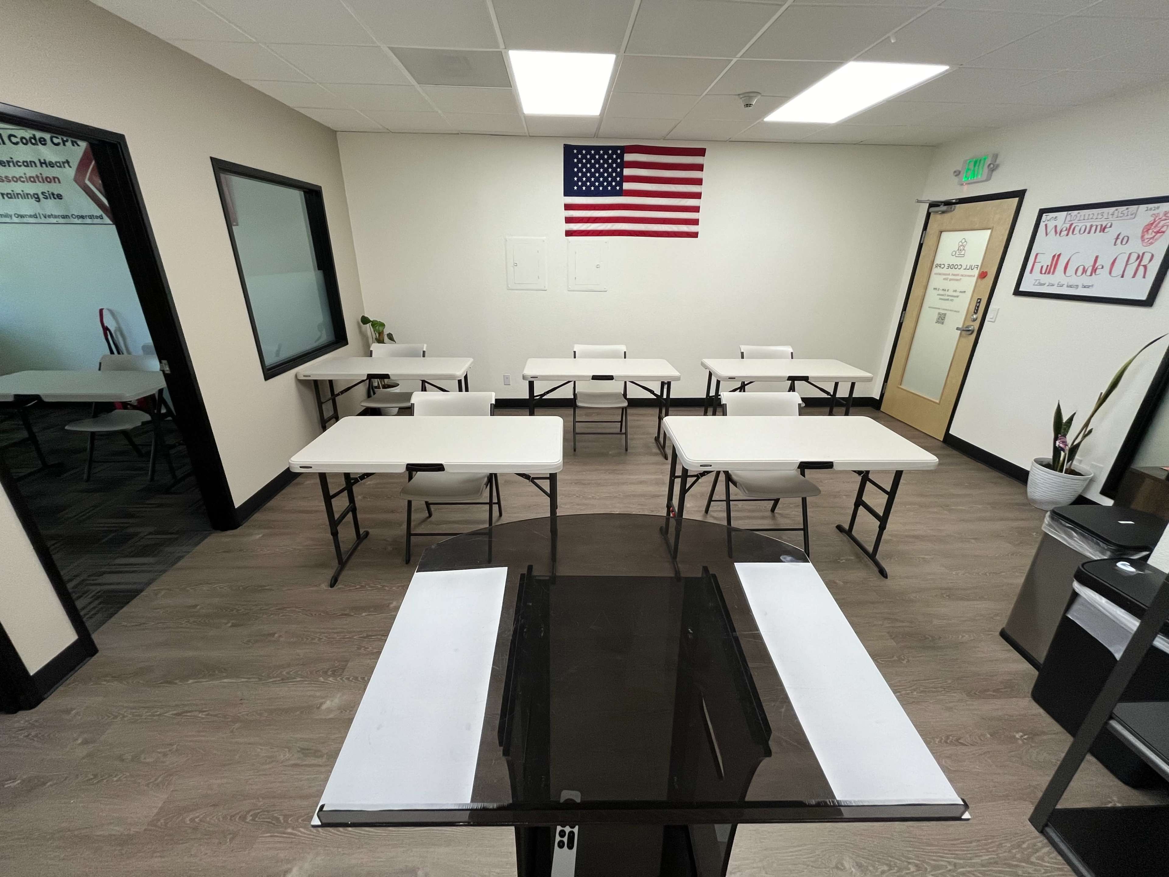 A classroom is set up with multiple tables and an American flag mounted on the wall.