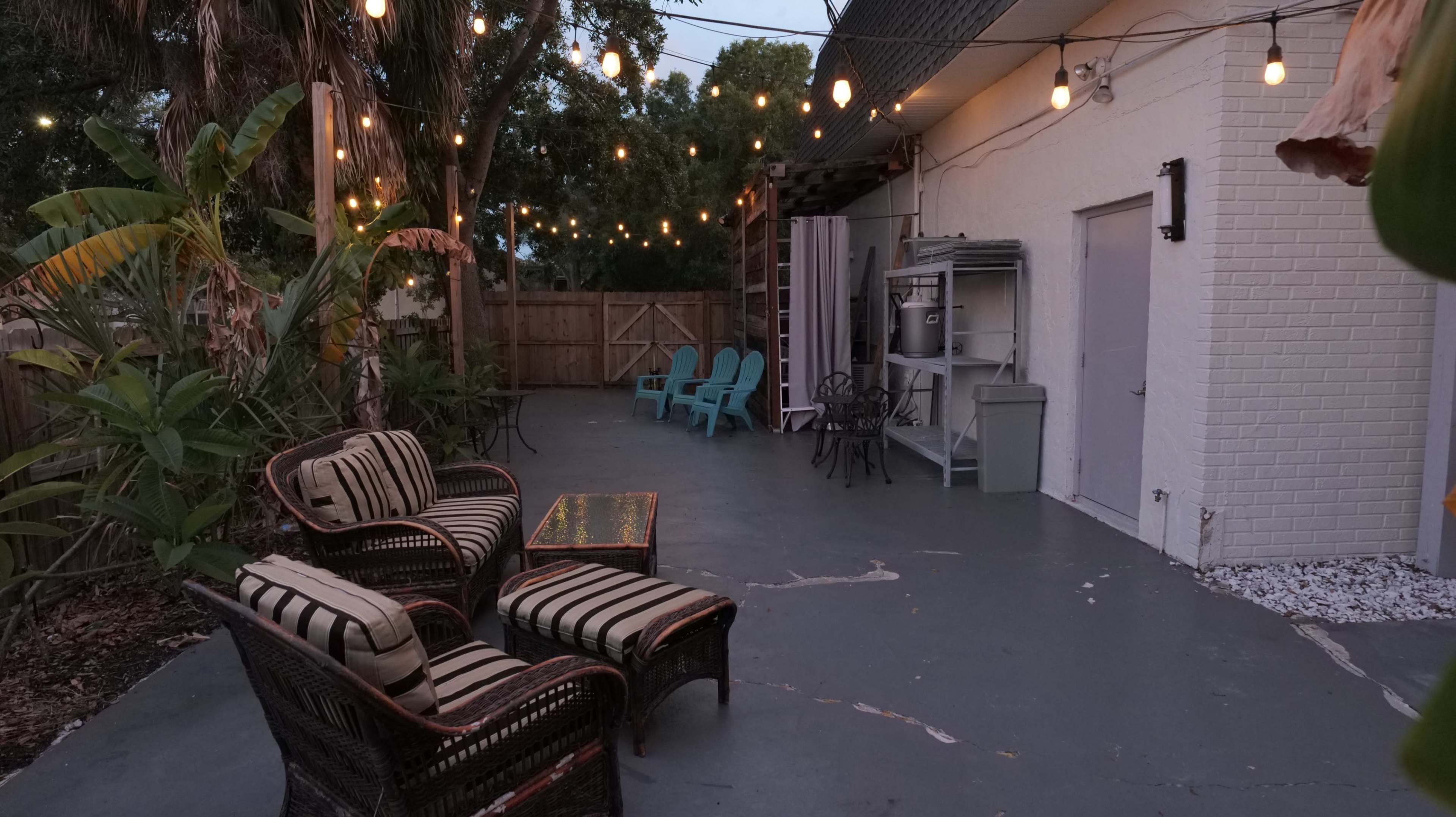 A patio area with string lights overhead, featuring a seating arrangement of wicker chairs and a small table on a concrete surface.