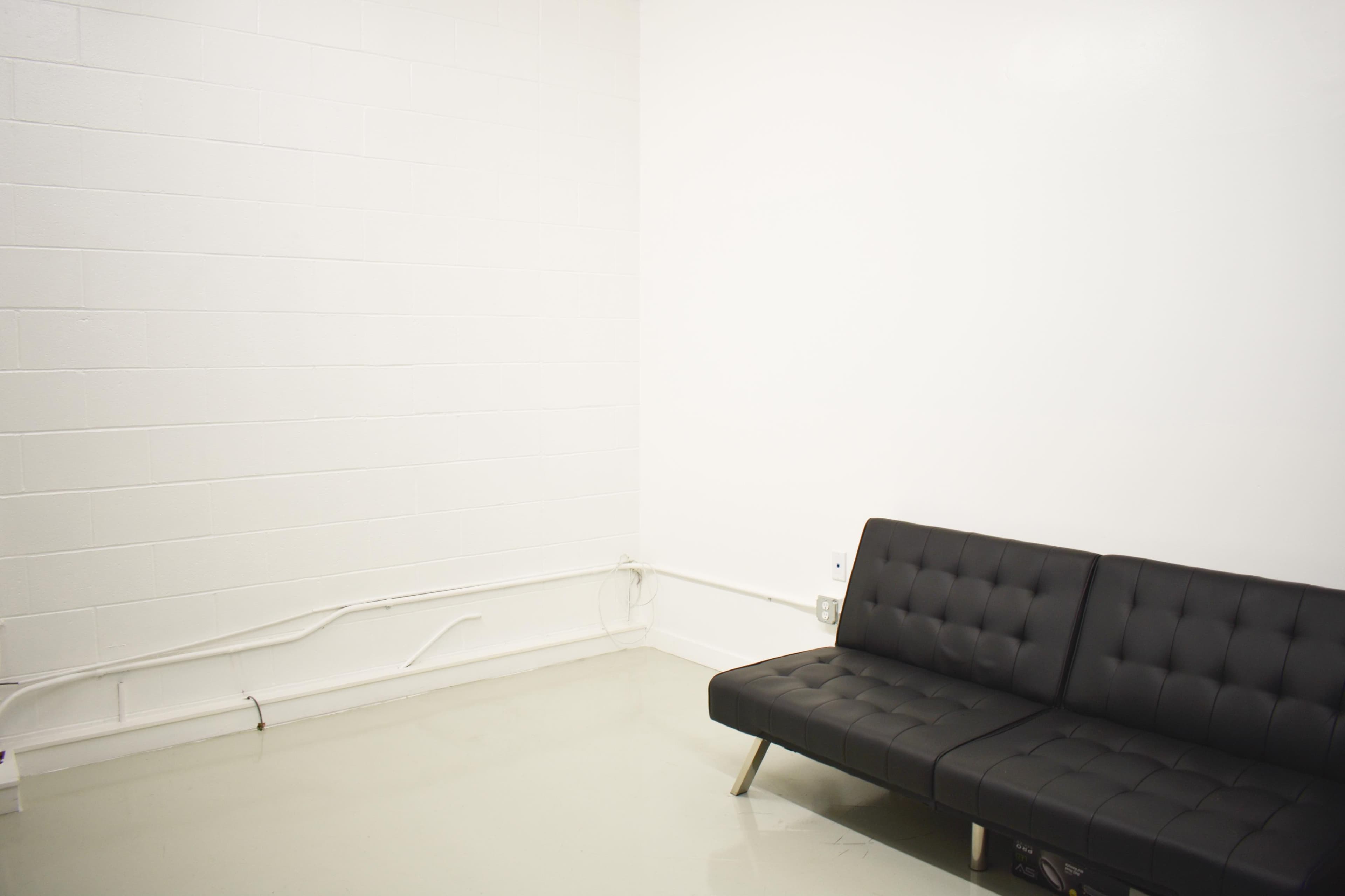 A black futon sofa against a plain white wall in a minimalistic room.