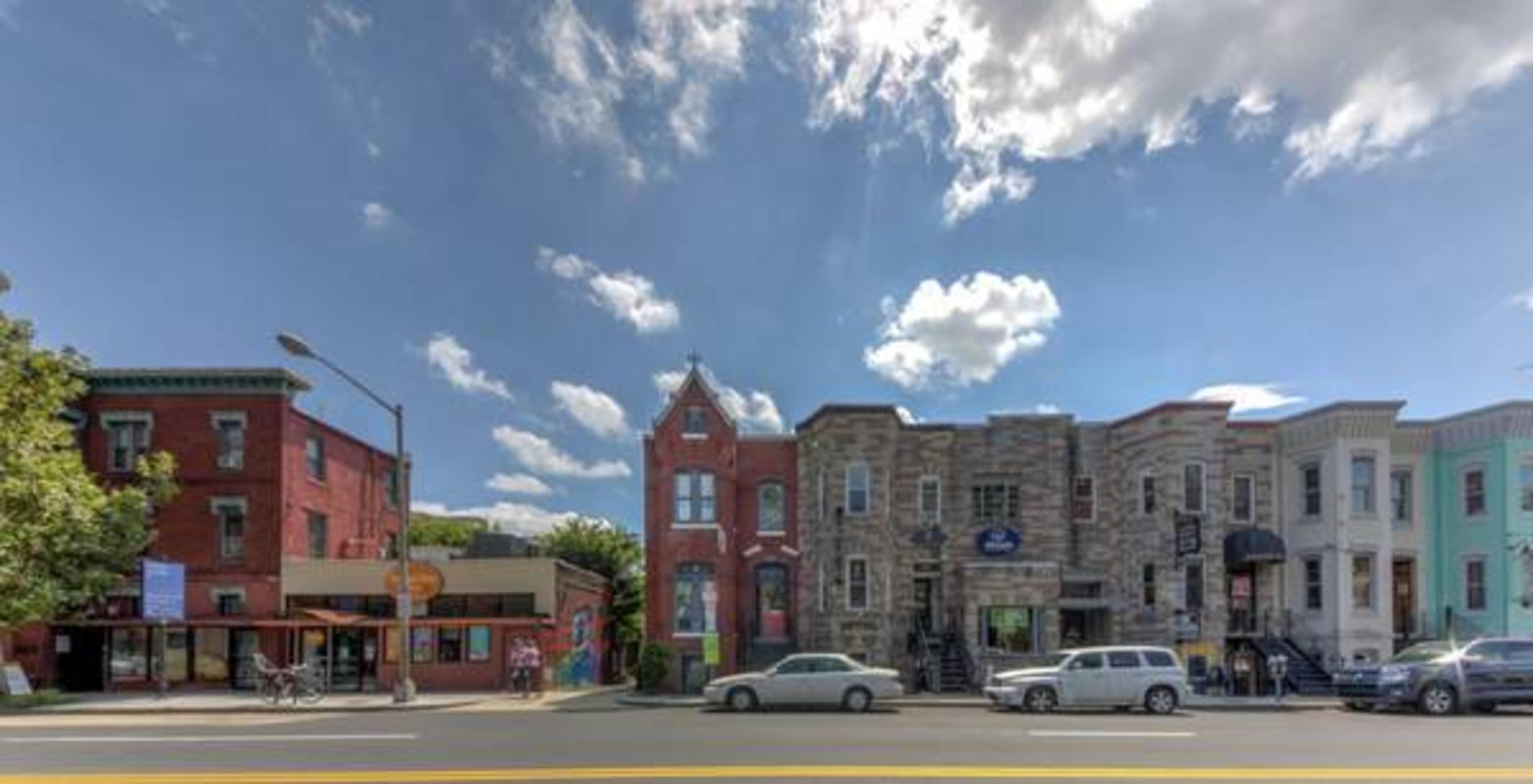 A row of buildings in varying architectural styles along a city street under a partly cloudy sky.