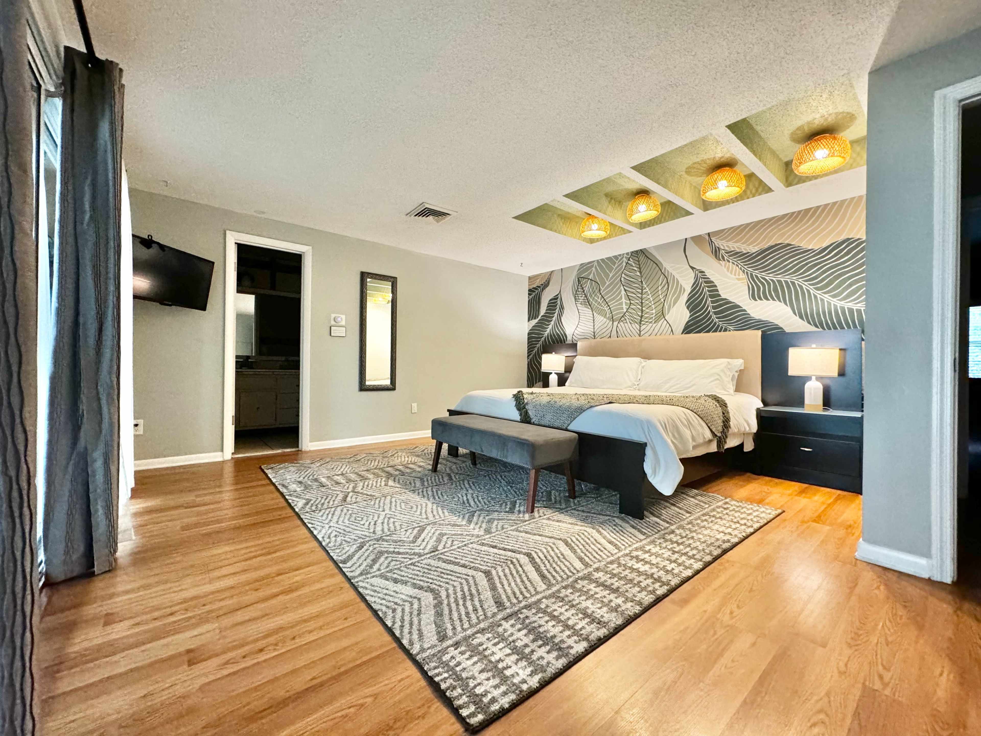 A spacious bedroom features a large bed, a patterned area rug, and decorative wall lighting.