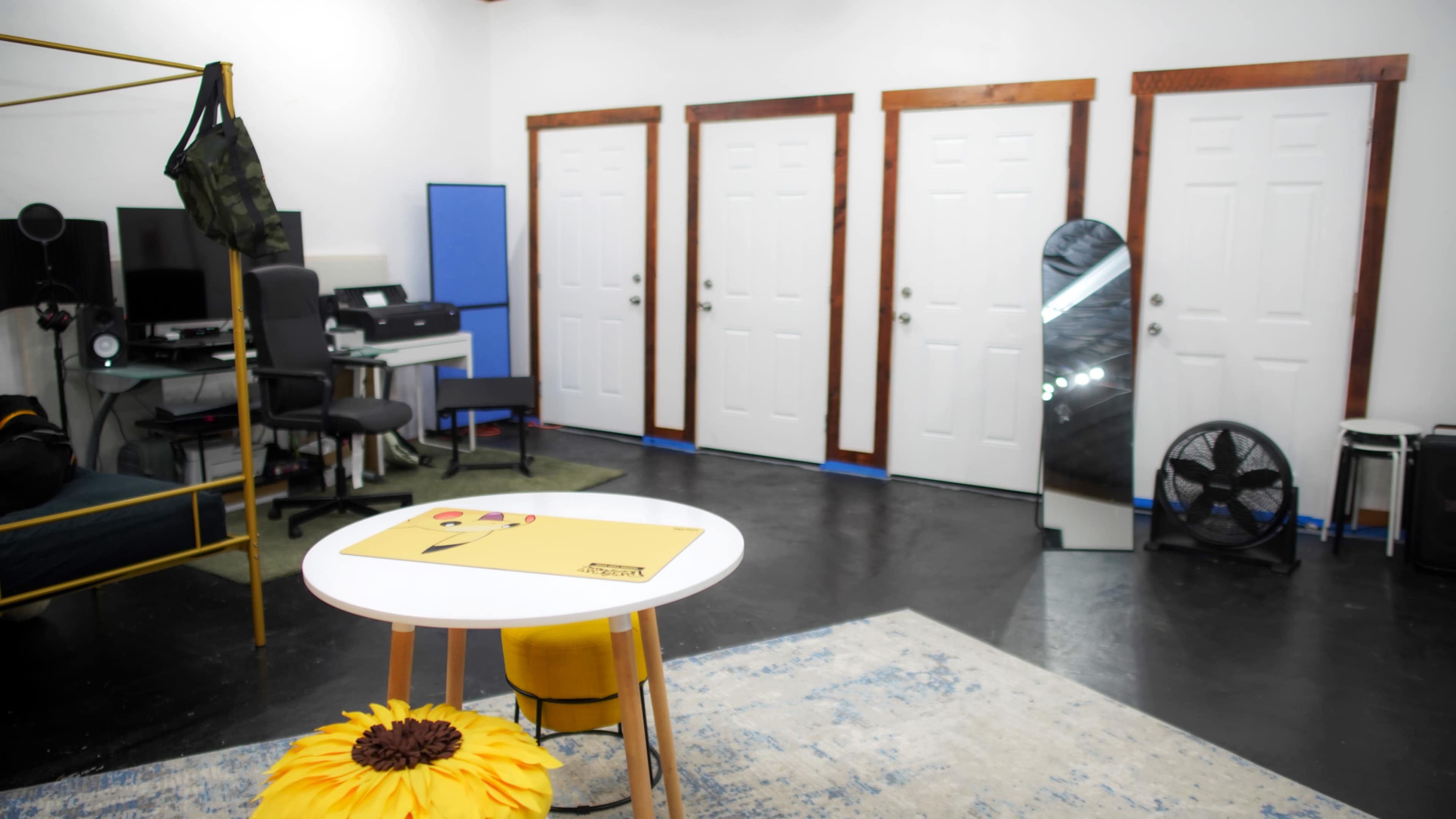 The image shows an interior space with four closed white doors, a circular table with a yellow placemat, a sunflower decoration, and a large mirror reflecting the room.