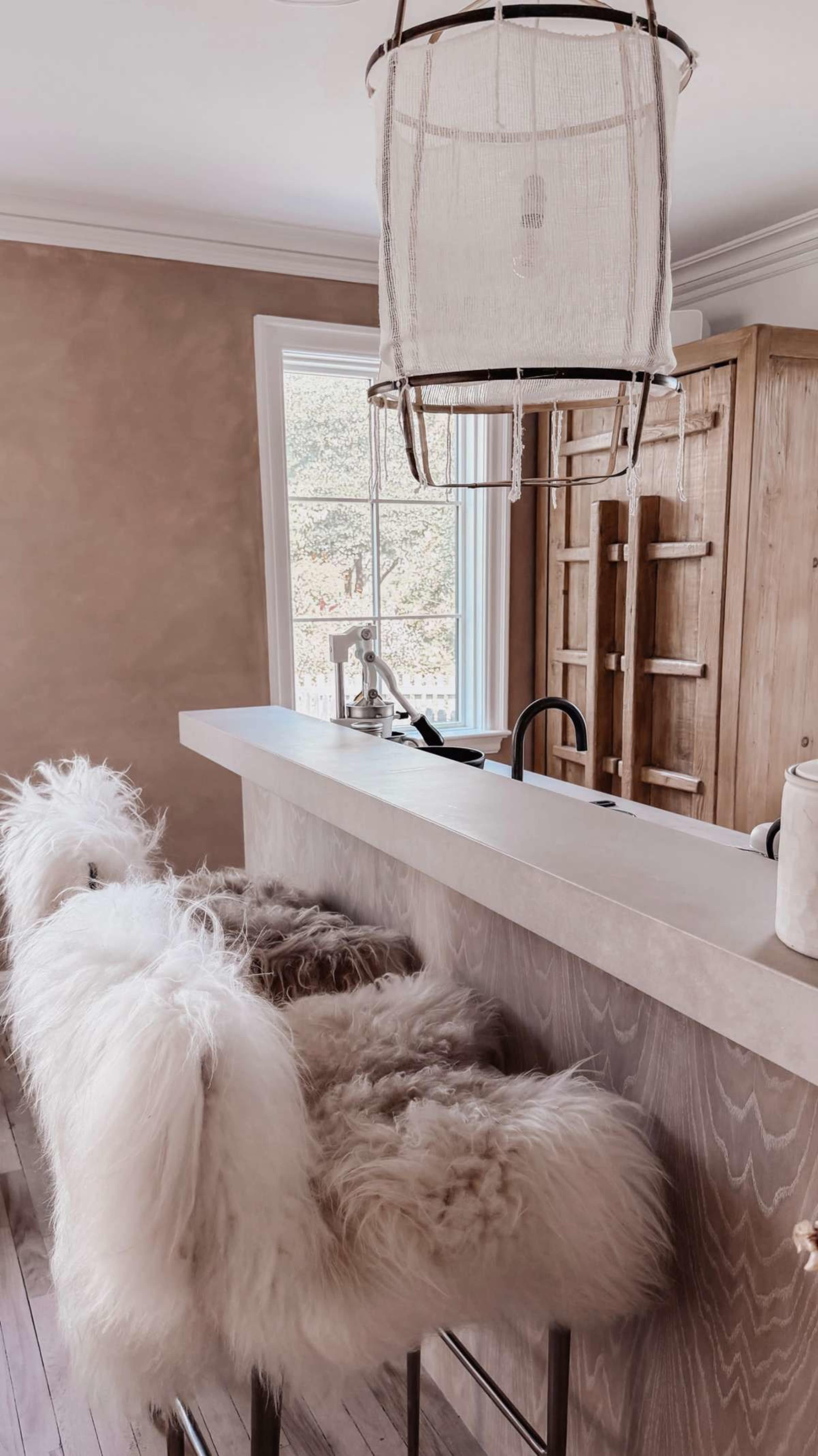 A kitchen bar area features stools with fur coverings and a stylish pendant light above.