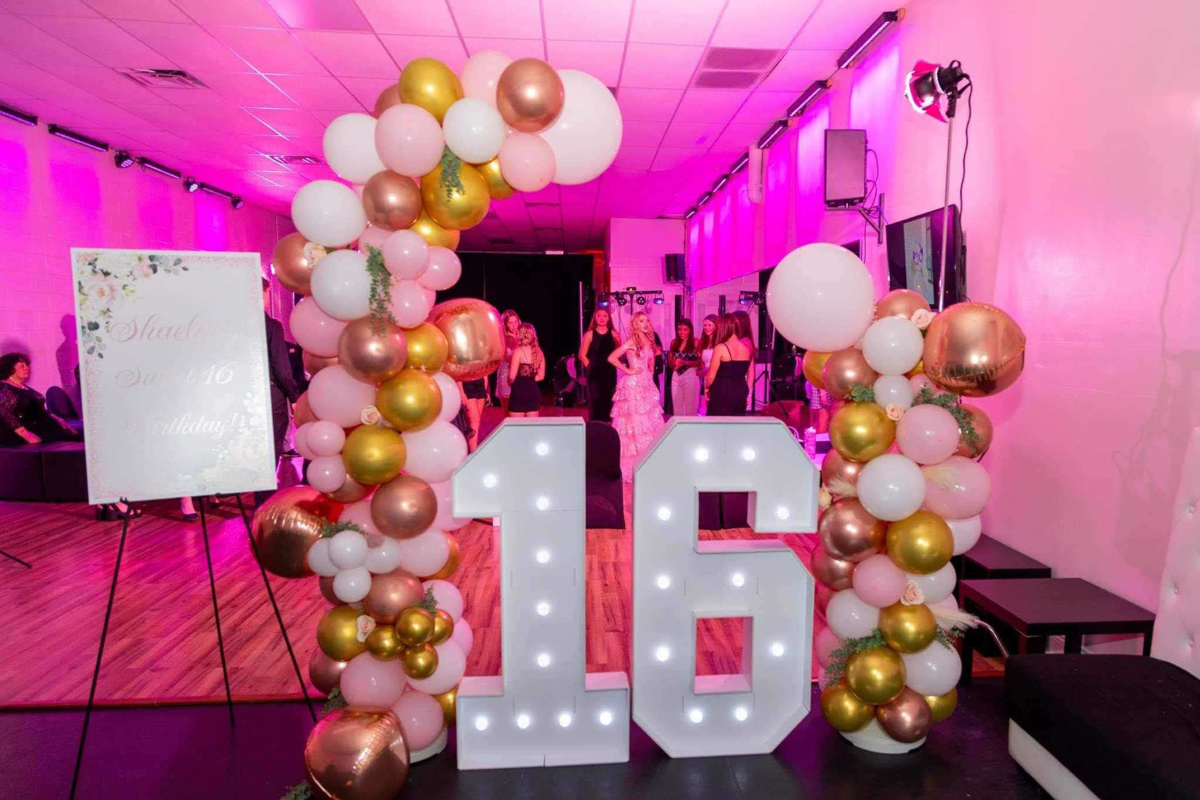 A large illuminated "16" surrounded by colorful balloons decorates an event space, while models walk the runway in the background.