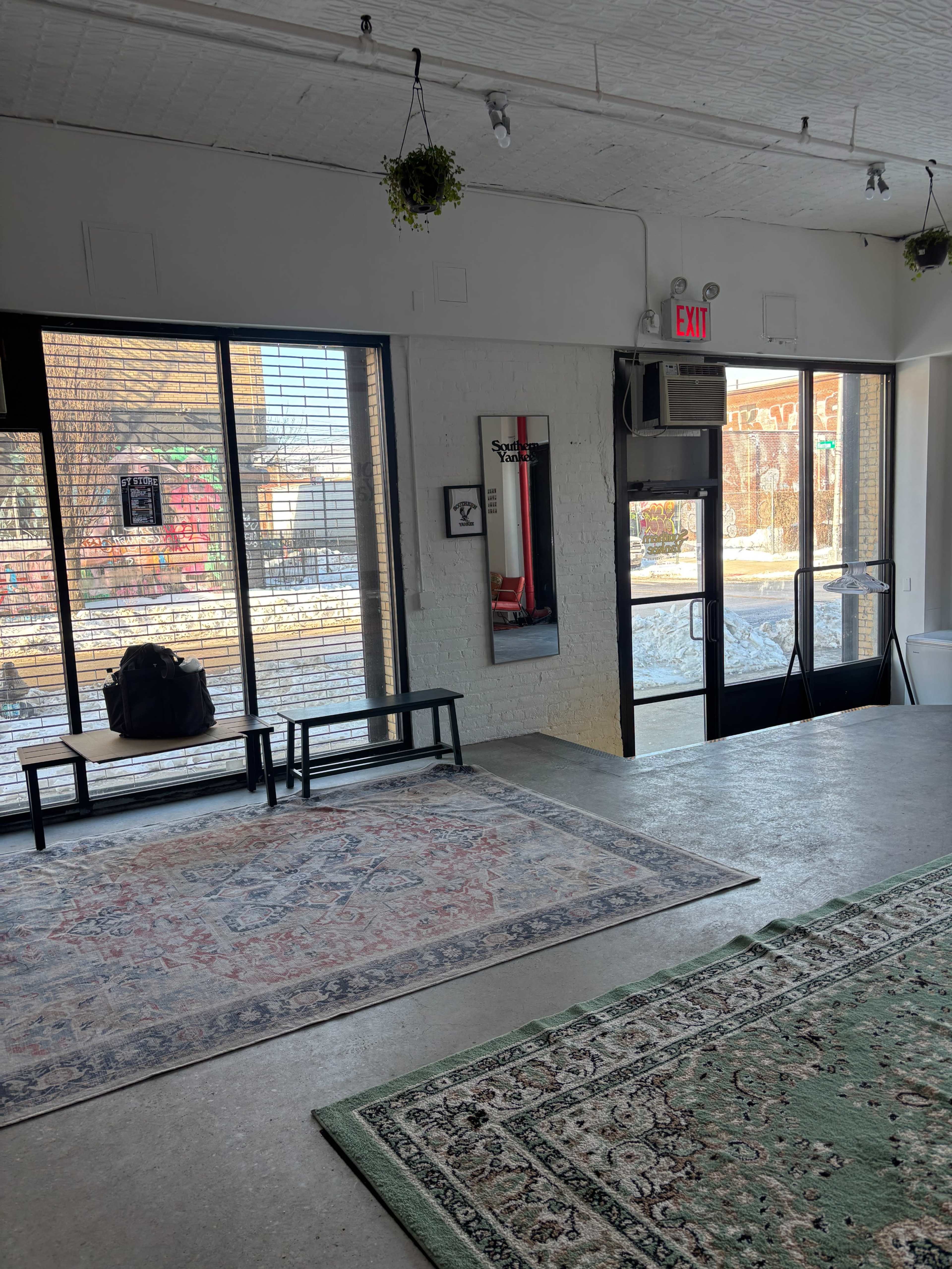 The image shows an interior space with two rugs, a bench, and large windows that provide a view of an outdoor area with snow.