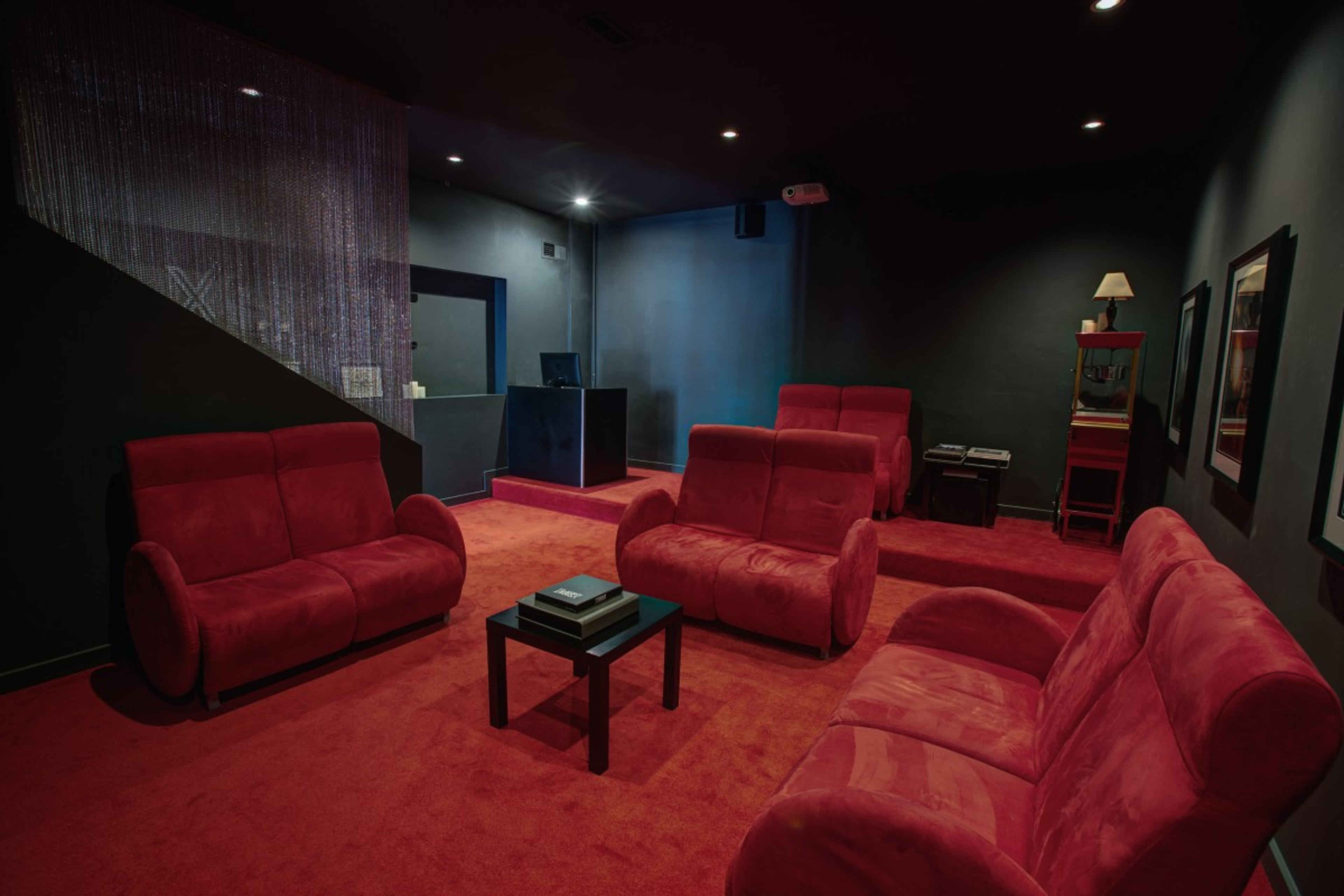 A dimly lit lounge area with four red couches arranged around a small black table on a red carpet.