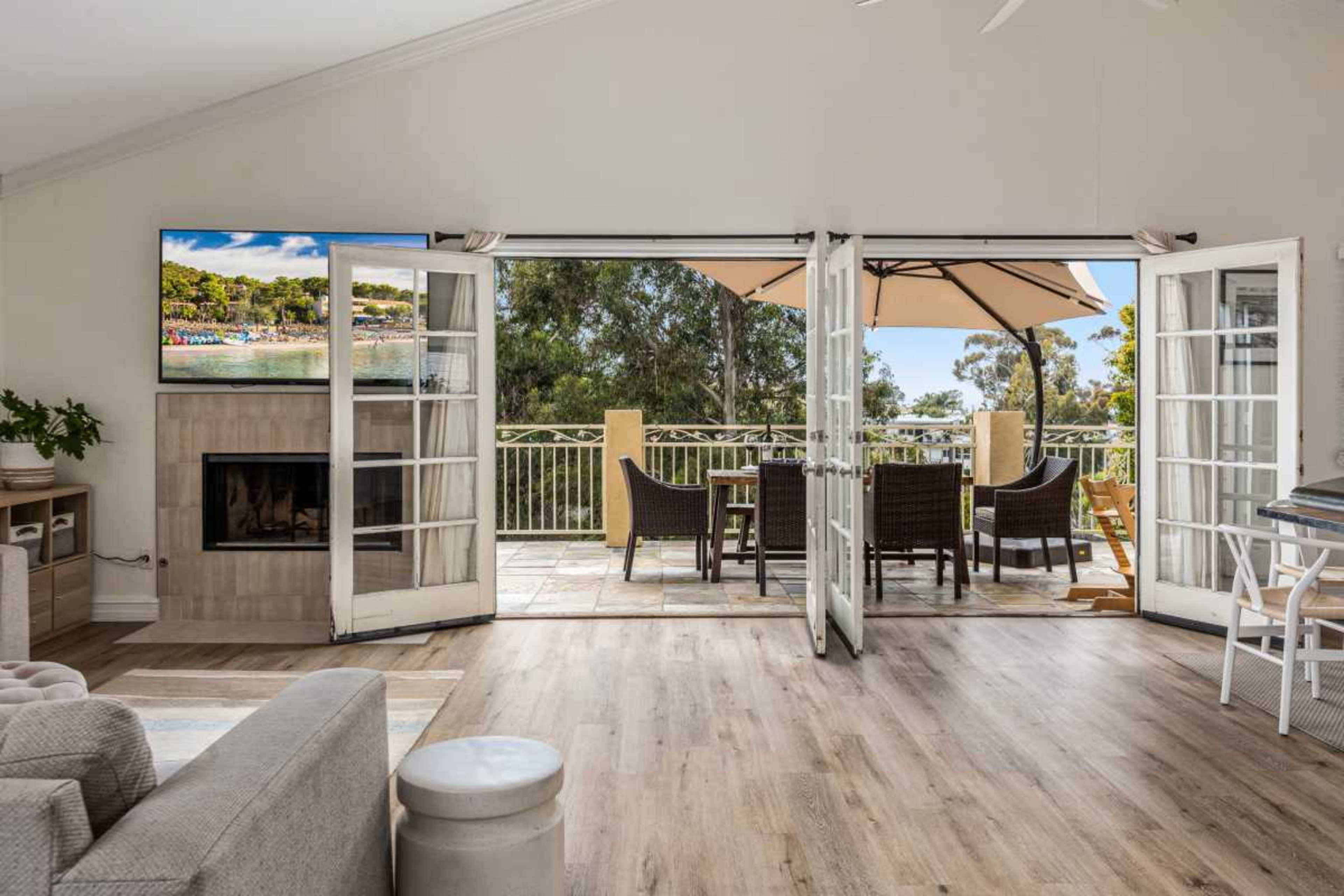 A living room features large open doors leading to a patio with outdoor furniture, overlooking a scenic view.