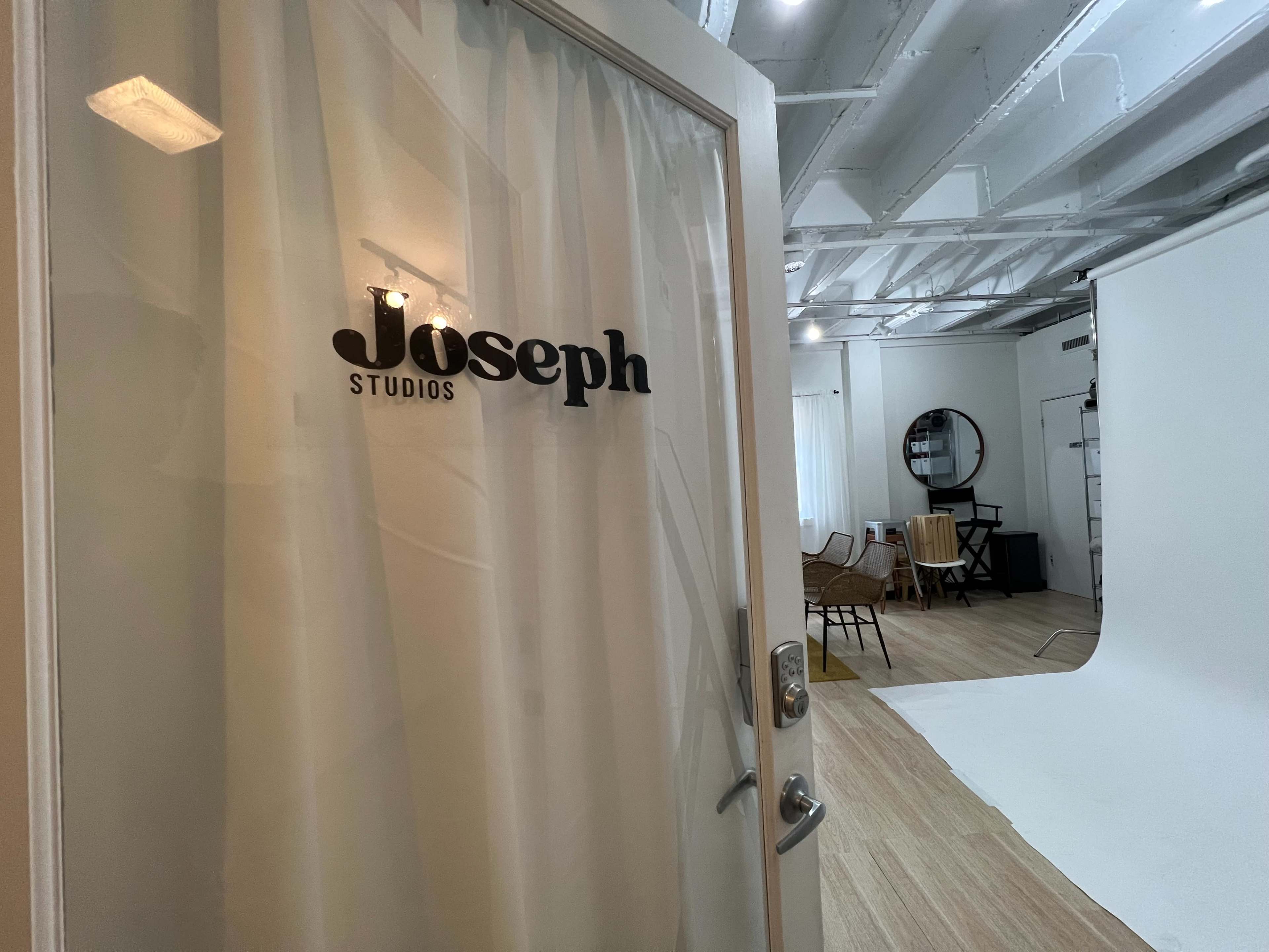 The entrance to Joseph Studios, featuring a door with a clear glass panel and a white curtain, leading into a studio space that includes a white backdrop and various chairs.