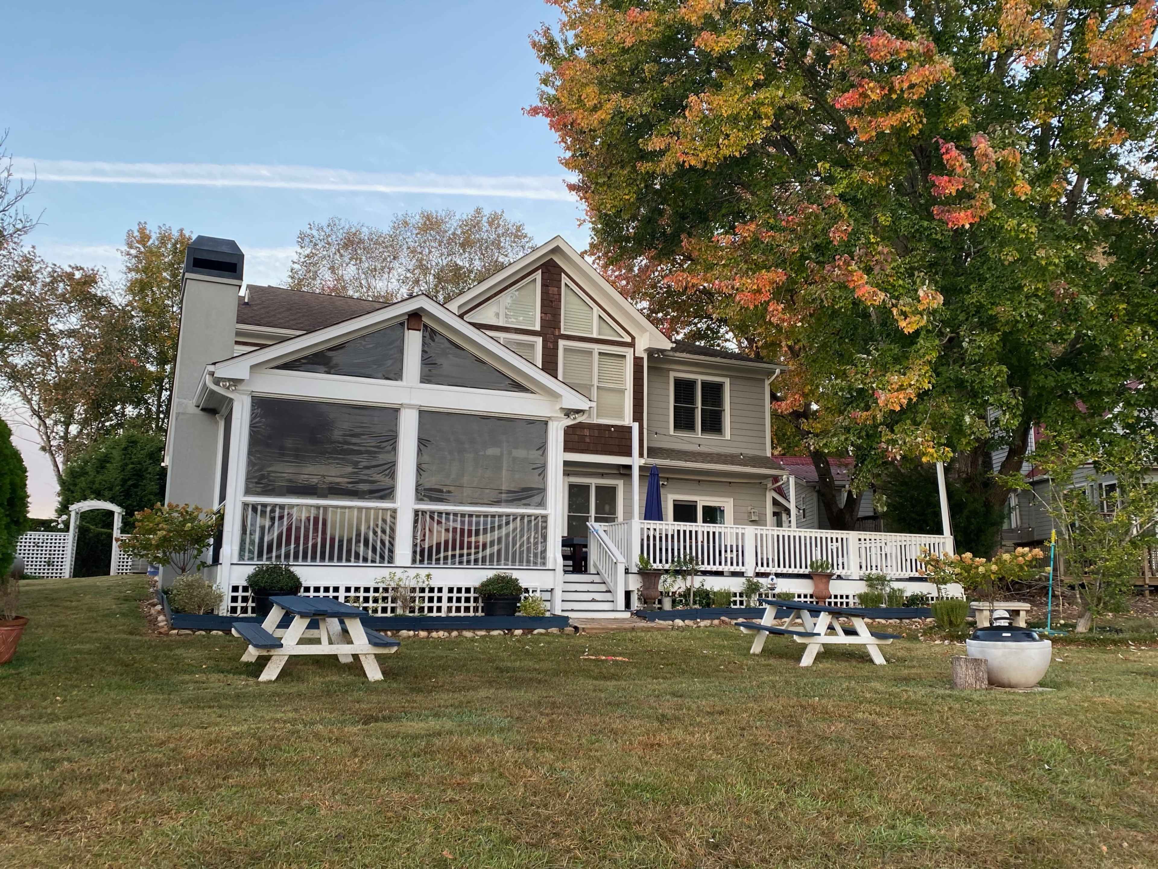 A modern two-story house with a screened porch and a large tree displaying autumn colors in the front yard.