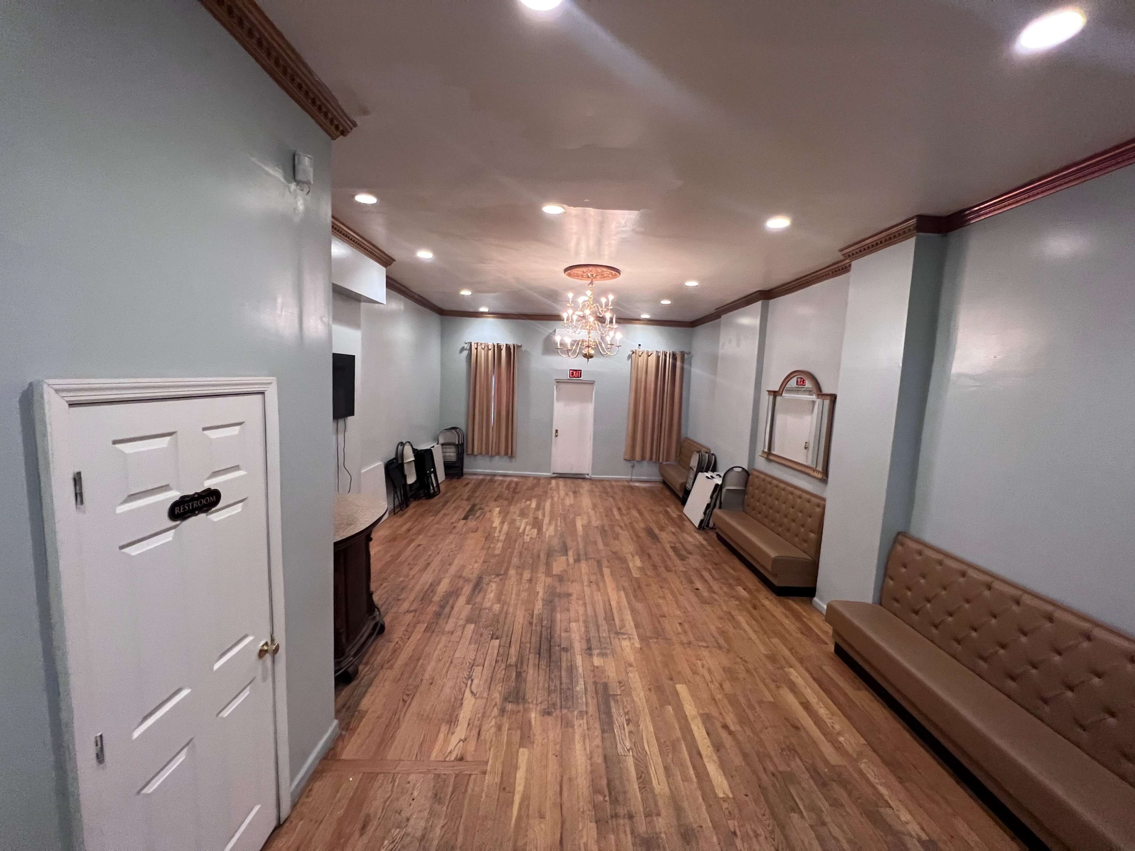 An interior room with light blue walls, hardwood flooring, a chandelier, and a row of tan benches along the walls.