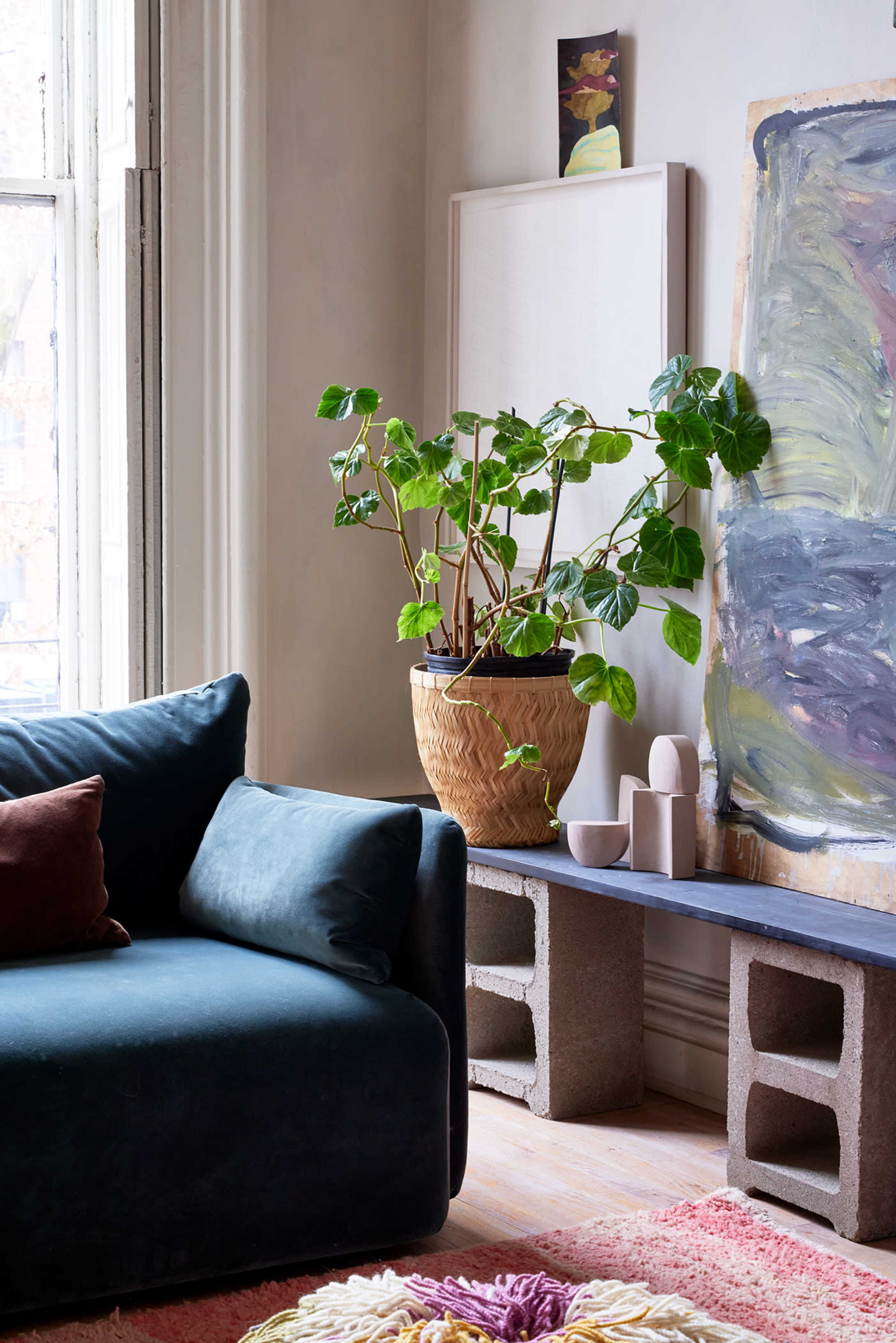 A spacious living room features a dark blue sofa next to a woven basket plant, complemented by a minimalist art piece and a textured rug.