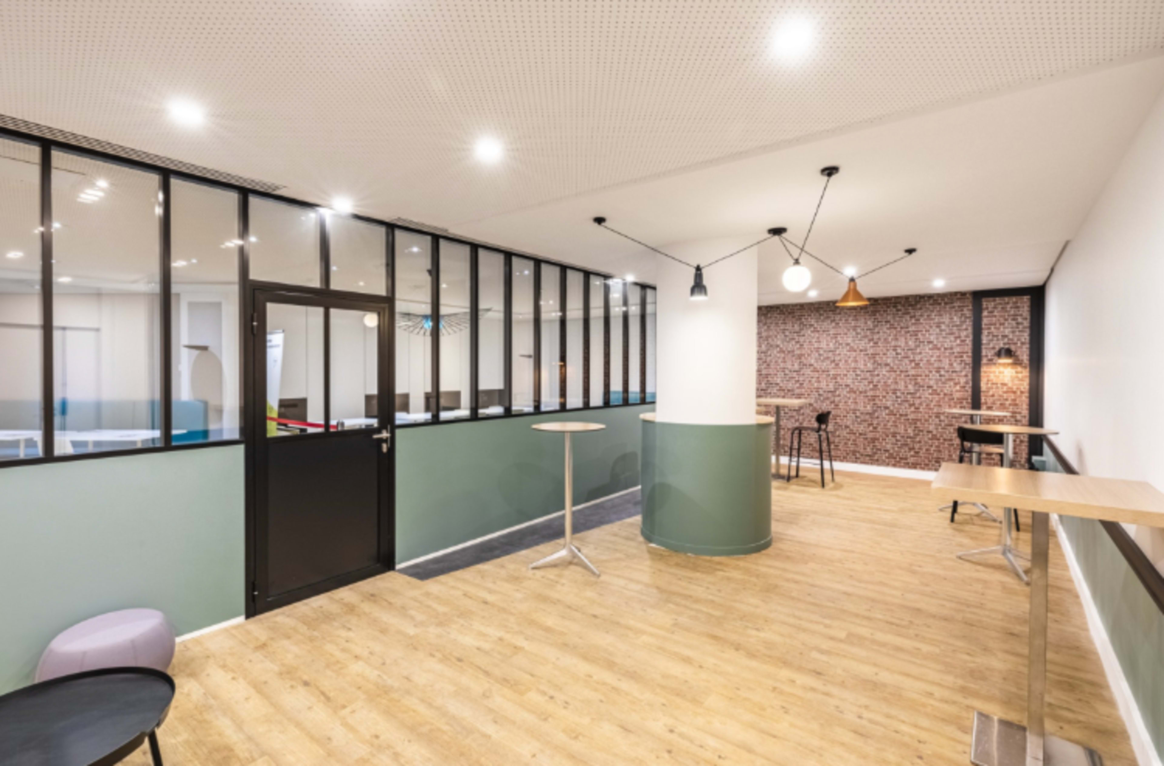 The image shows a modern, open office space featuring a mix of glass partition walls, wooden accents, and a combination of seating arrangements.