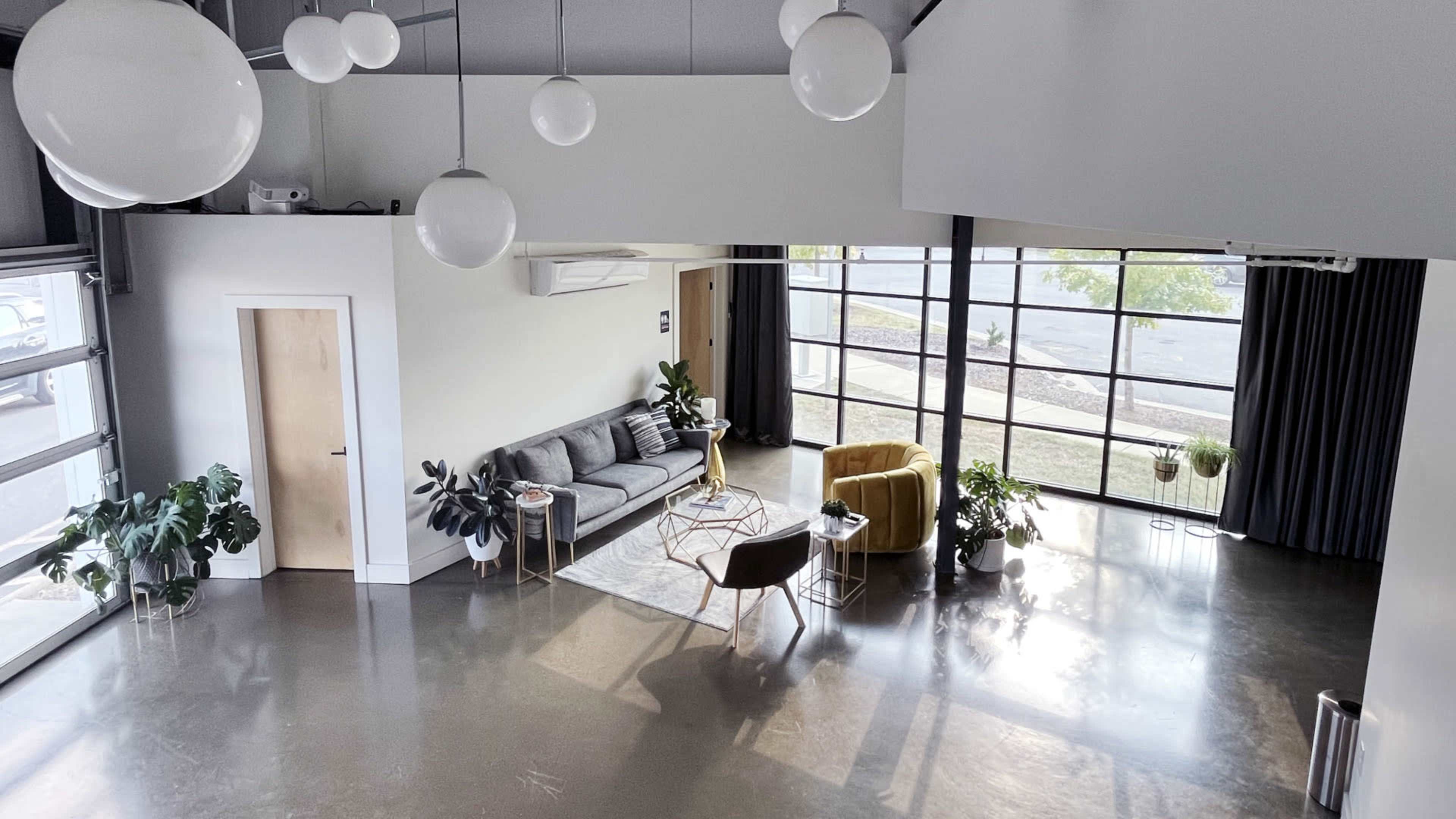 The interior features a modern lounge area with a gray sofa, a yellow armchair, and large windows allowing natural light to fill the space.