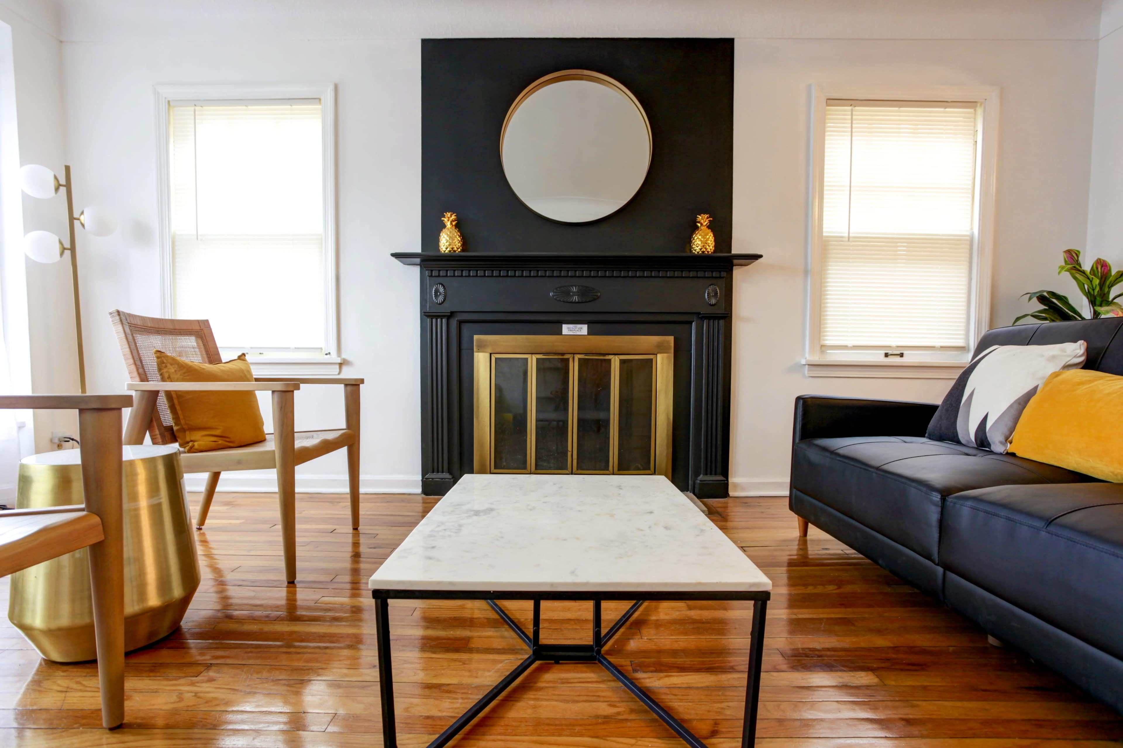 A modern living room with a black fireplace, a round mirror above it, a marble-top coffee table, and wooden floors.