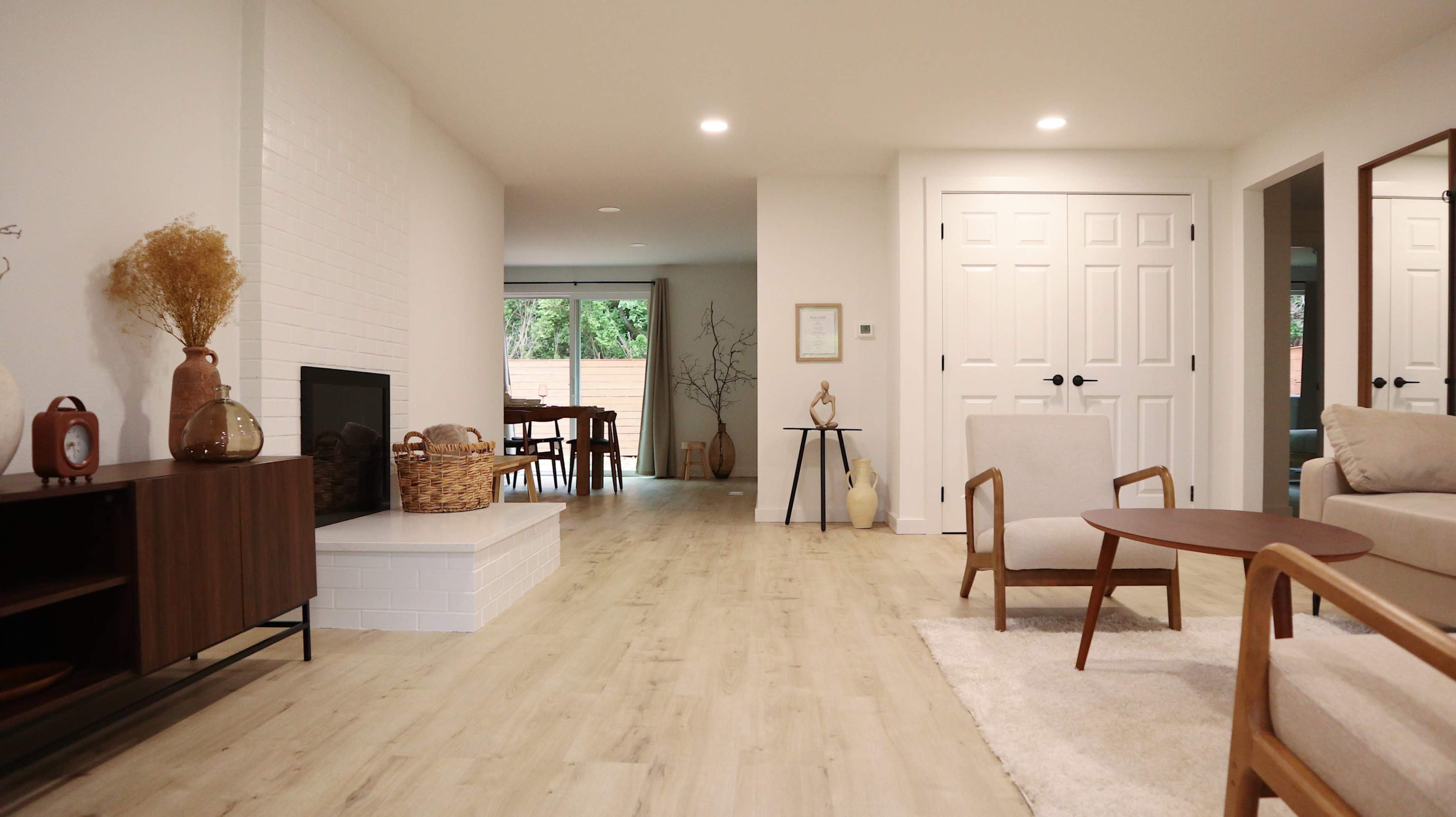 A modern interior living space with a light-colored wooden floor, a fireplace, a table set for dining, and two chairs positioned around a coffee table.